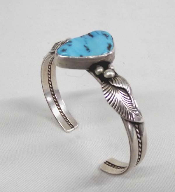 Navajo Sterling and Turquoise Bracelet by Nez: Native American Navajo Sterling and Turquoise Bracelet by Nez. Large polished turquoise nugget is framed by traditional silver work of leaves and beads. Two band bracelet with rope embellishment in th