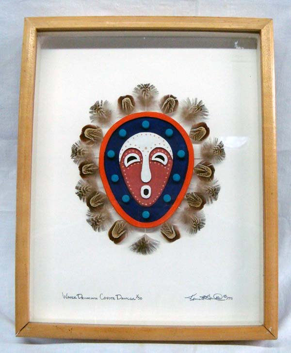 Framed Kumeyaay Water Drinking Mask by Kenneth Banks: Ceramic Mask-Water Drinking Coyote Dancer - Banks. This is a ceramic mask with feathers surrounding it, glued to a backing board and in a deep wood frame, under glass. It is signed by the artist, ''Ke