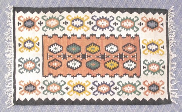 Kilim Rug: Kilim Rug. Wool rug in light tan background with several figures of pumpkin color, dark green, rust, blue and other colors. Some worn spots and needs cleaning. Measures 63''Lx39''W.