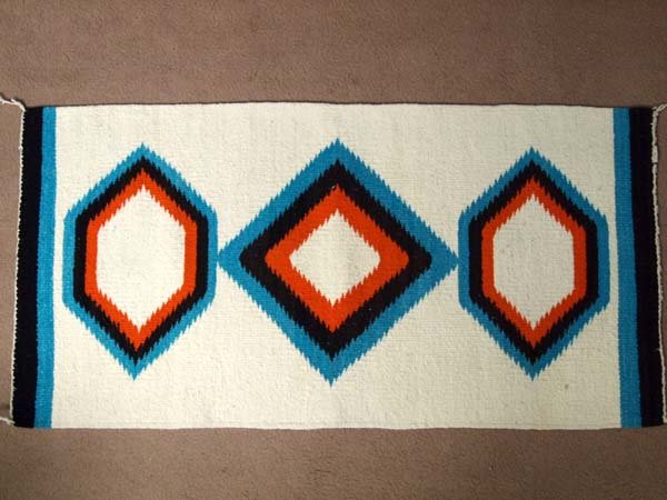 Navajo Weaving: Navajo Weaving. 36.5'' L x 19'' W. Three geometric designs. Off white with turquoise, orange and black. Some small staining, but overall in clean condition.