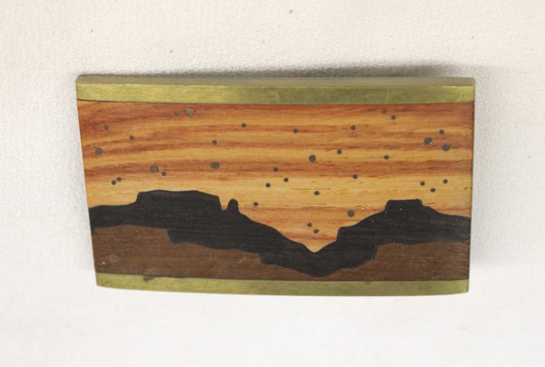 1982 Brass and Wood Inlay Belt Buckle: 1982 Brass and Wood Inlay Belt Buckle, features sunset in Monument Valley, hallmarked on back and also reads Cuba, New Mexico 1982. Measures approx. 2 1/2"L x 1 1/2"W.