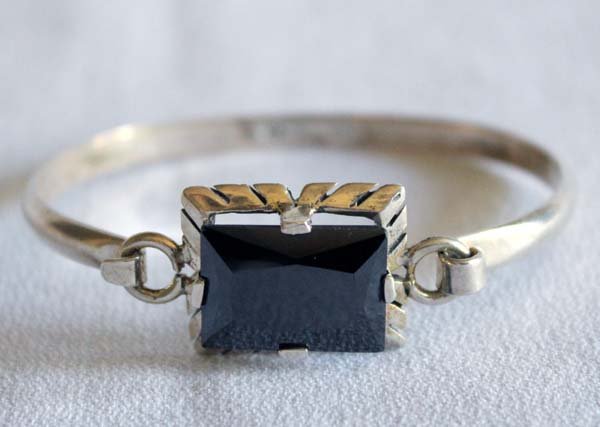 Taxco Sterling Silver Obsidian Hinged Bracelet: Taxco Sterling Silver Obsidian Hinged Bracelet, inside measures 6.5'' x .75''W, sterling silver bangle bracelet with hinged clasp set with a faceted obsidian gemstone, stamped .925 JL-JJ, 20.64g in to