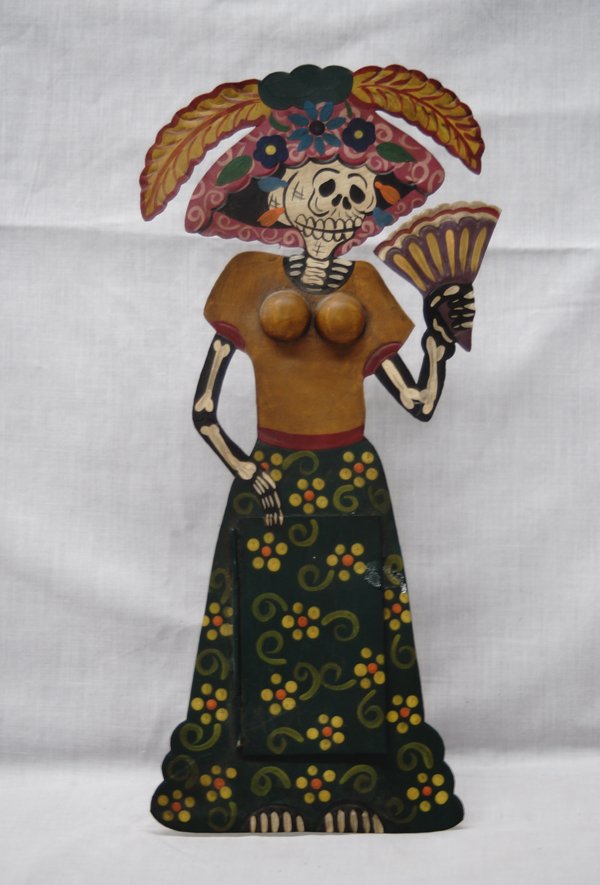 Mexican Tin Female Day of the Dead Skeleton Mirror: Mexican Tin Female Day of the Dead Skeleton Mirror, cut and hand painted tin, stand built into back, also has loop on back for hanging, measures 13''H x 6''W