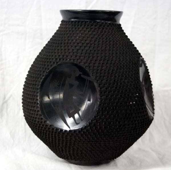 Mexican Mata Ortiz Black on Black Jar by Gonzalez: Mexican Mata Ortiz Black on Black Kokopelli Jar by Jose Gonzalez, signed by artist and measures 9.5''H x 9''D, predominantly textured body, flared rim, features 4 gun metal finished concave kokopelli 