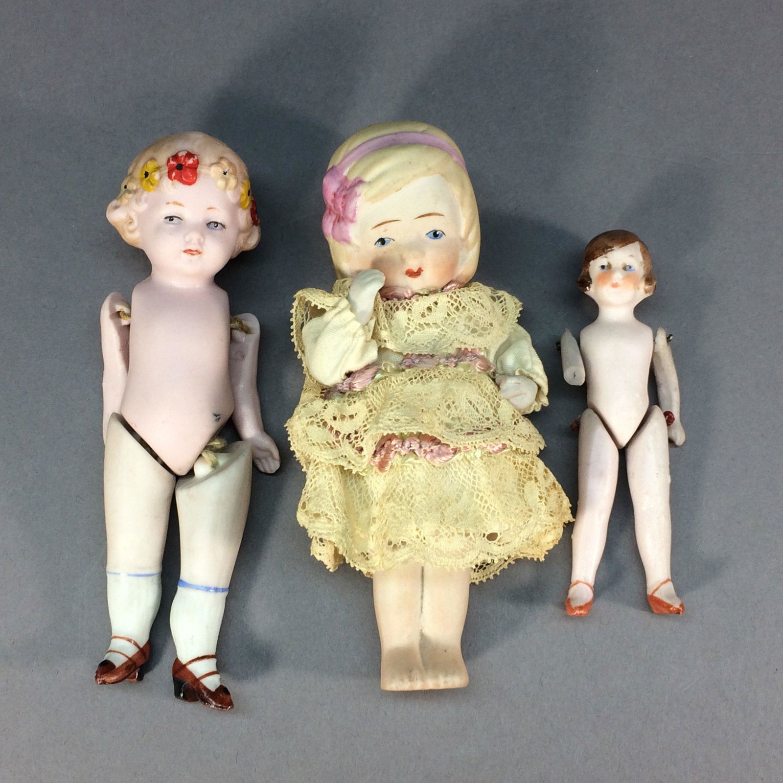 Three All Bisque Dolls – Germany and Nippon: Lot of three all bisque dolls. The girl with the molded flowers in her hair is pink bisque and is incised Germany on her back. Her legs are not original, they look like they came from an earlier doll.
