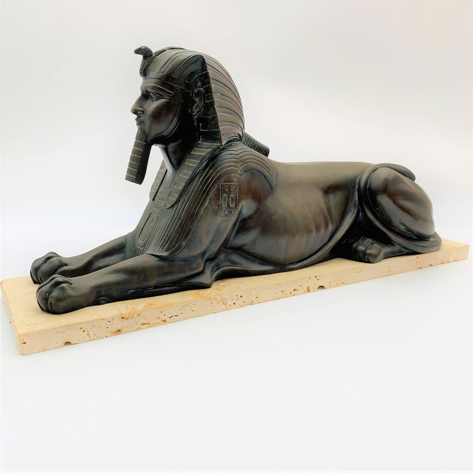 Antique Egyptian Revival Bronze Sculpture: Antique Egyptian Revival Bronze Sculpture of a Sphinx Mounted on a later travertine Stone Base. Unmarked. Sculpture measures 7-1/4" H x 15" L, altogether measures 7-5/8" H x 16-5/8" W x 4-5/8" D