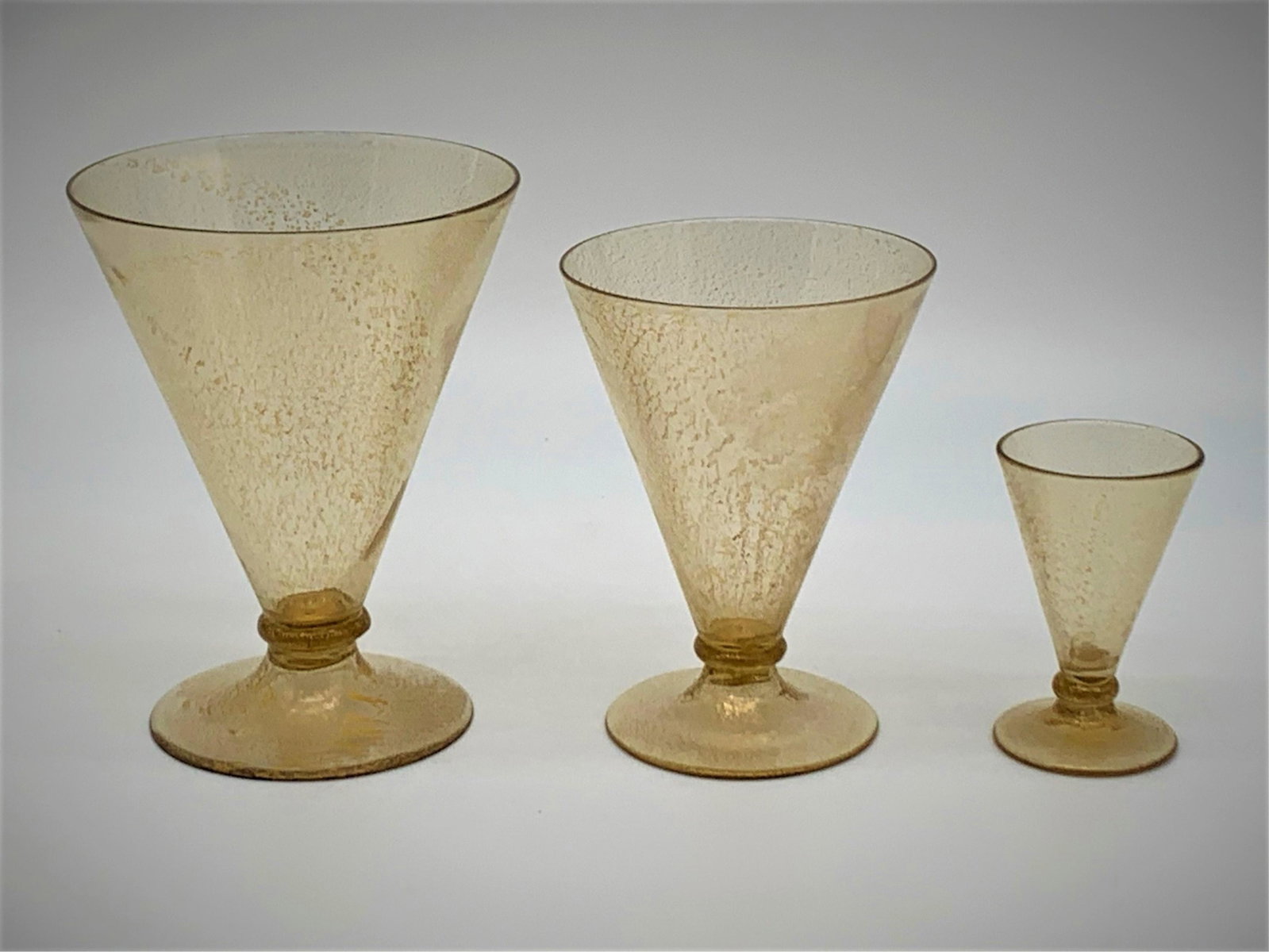 21 Pcs Mid Century Italian Gold and Clear Glasses: 21 Pcs Mid Century Italian Gold and Clear Barware Glasses. Possibly Venini. V shaped with gold flecks throughout the clear glasses. Unsigned. The set includes: 7 water glasses 5", 8 wine glasses 4", 6