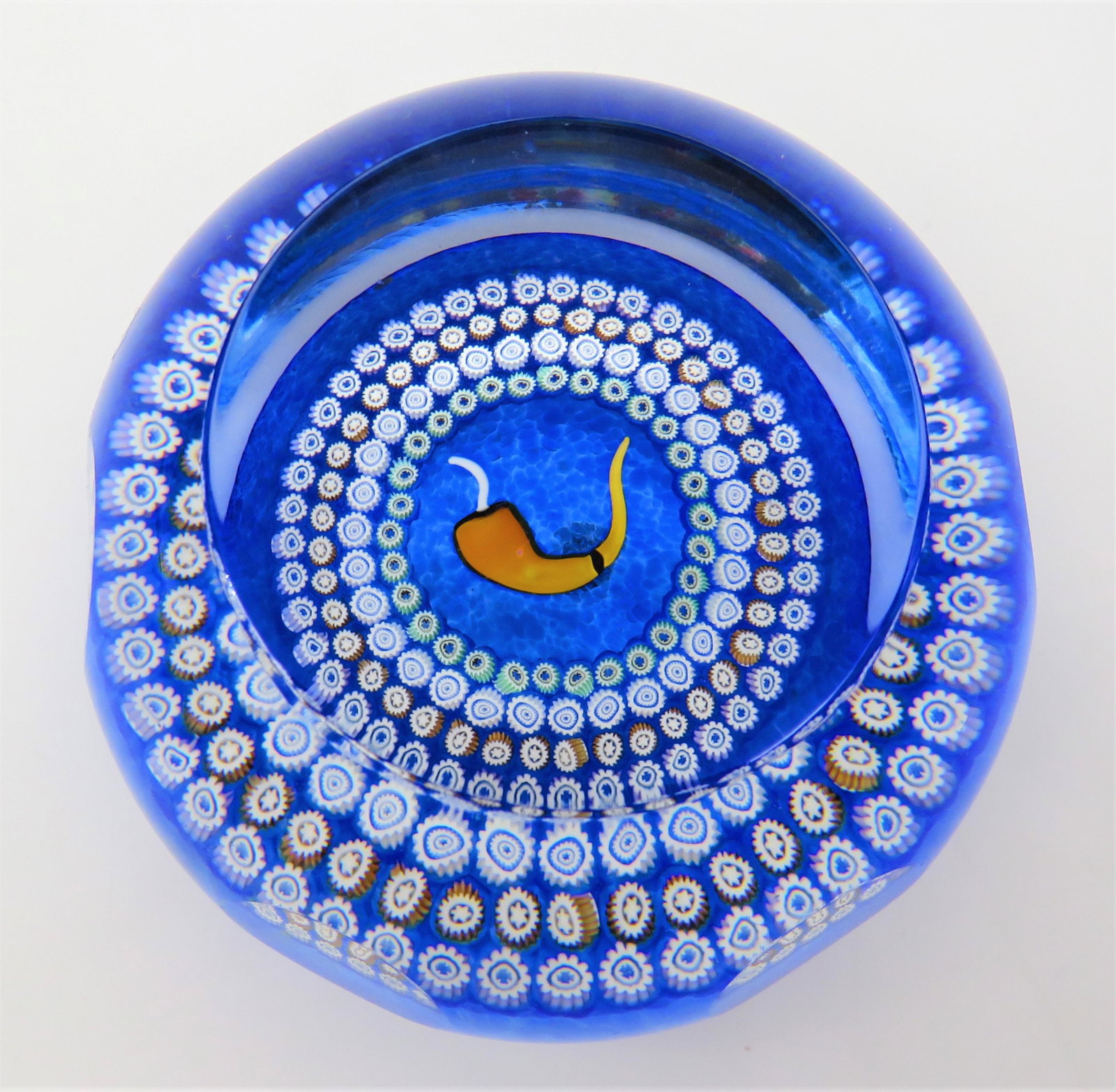 Caithness Scotland Chili Pepper Glass Paperweight: Caithness Scotland Chili Pepper Glass Paperweight. The cased glass weight with indentations on sides, pepper form surrounded by canes on blue ground. 1987 date cane and clear label on bottom. Very goo