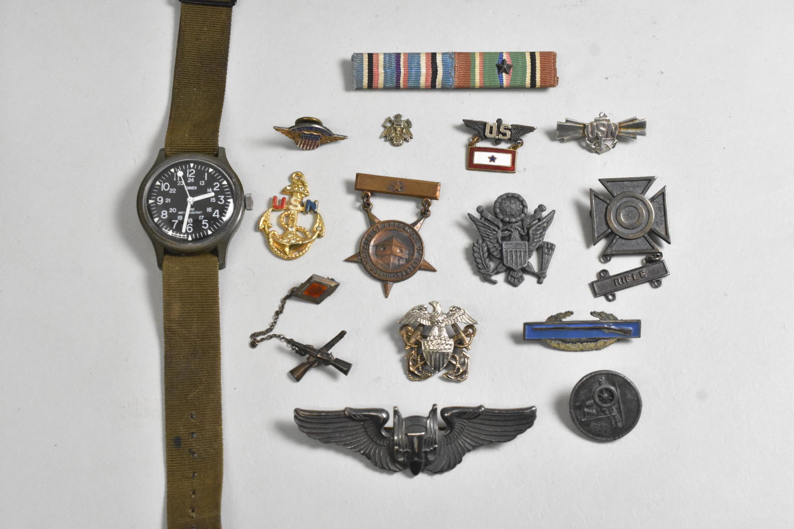 Sterling Bombadier Wings Timex Military: Lot of misc. military items. Sterling bombadier wings. USA anchor pendant. Sterling rifle "X". Variety of medals, 8 marked sterling. Uniform button. Timex water resistant watch, runs.