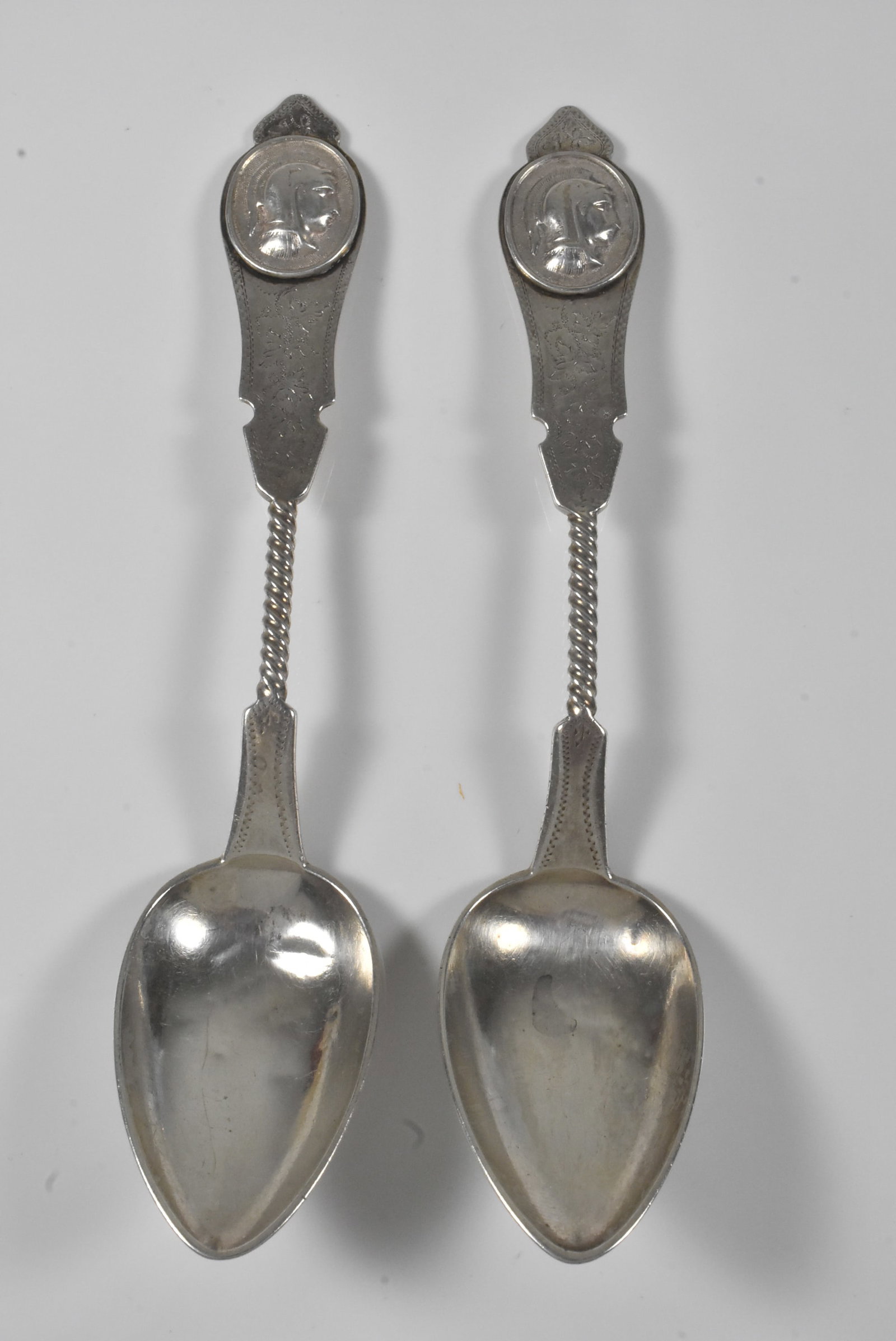Duhme Medallion Coin Silver Twisted Handle Spoons: Two Duhme coin silver spoons with Medallion pattern and twisted handles. 6 3/8". 59.2g. Both are engraved. 1 is dented.