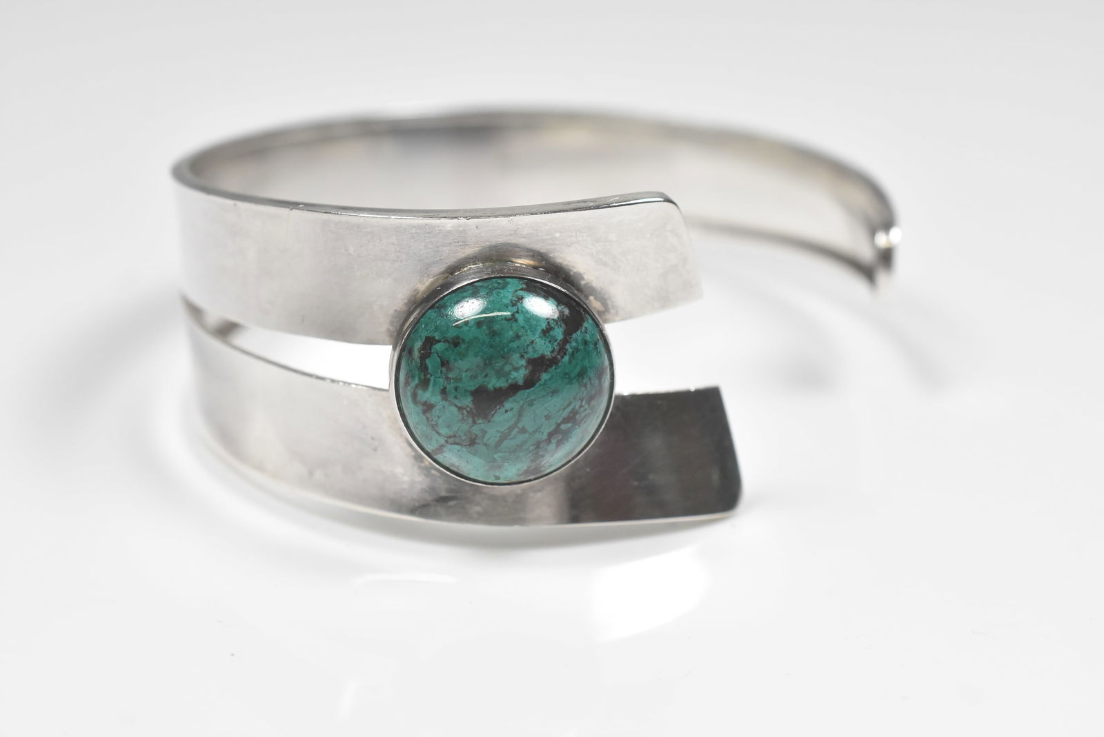 Modern Cuff Bracelet: Cuff bracelet in a modern asymetrical design with bluish green round stone. Not marked. 6 1/2" with 1 1/4" gap. 27.1g