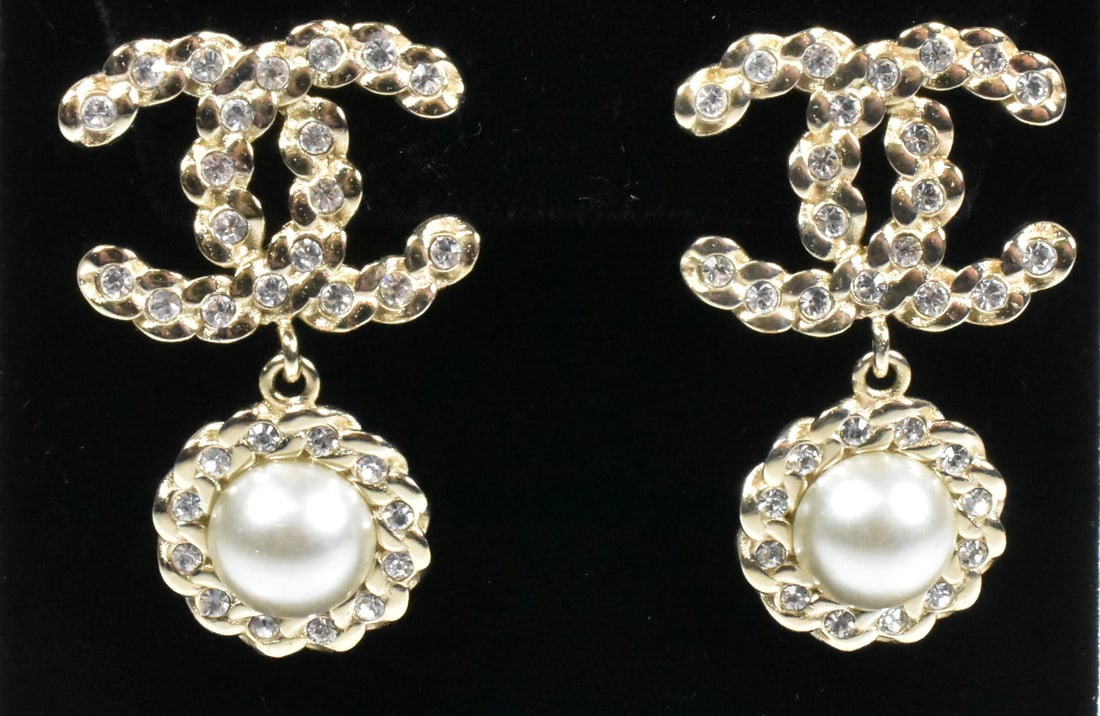 Chanel Pearl and Rhinestone Earrings: Chanel pierced earrings in gold tone with double C design and pearl drop surrounded by braided detail and covered in rhinestones. 1 1/4" long x 7/8" wide.