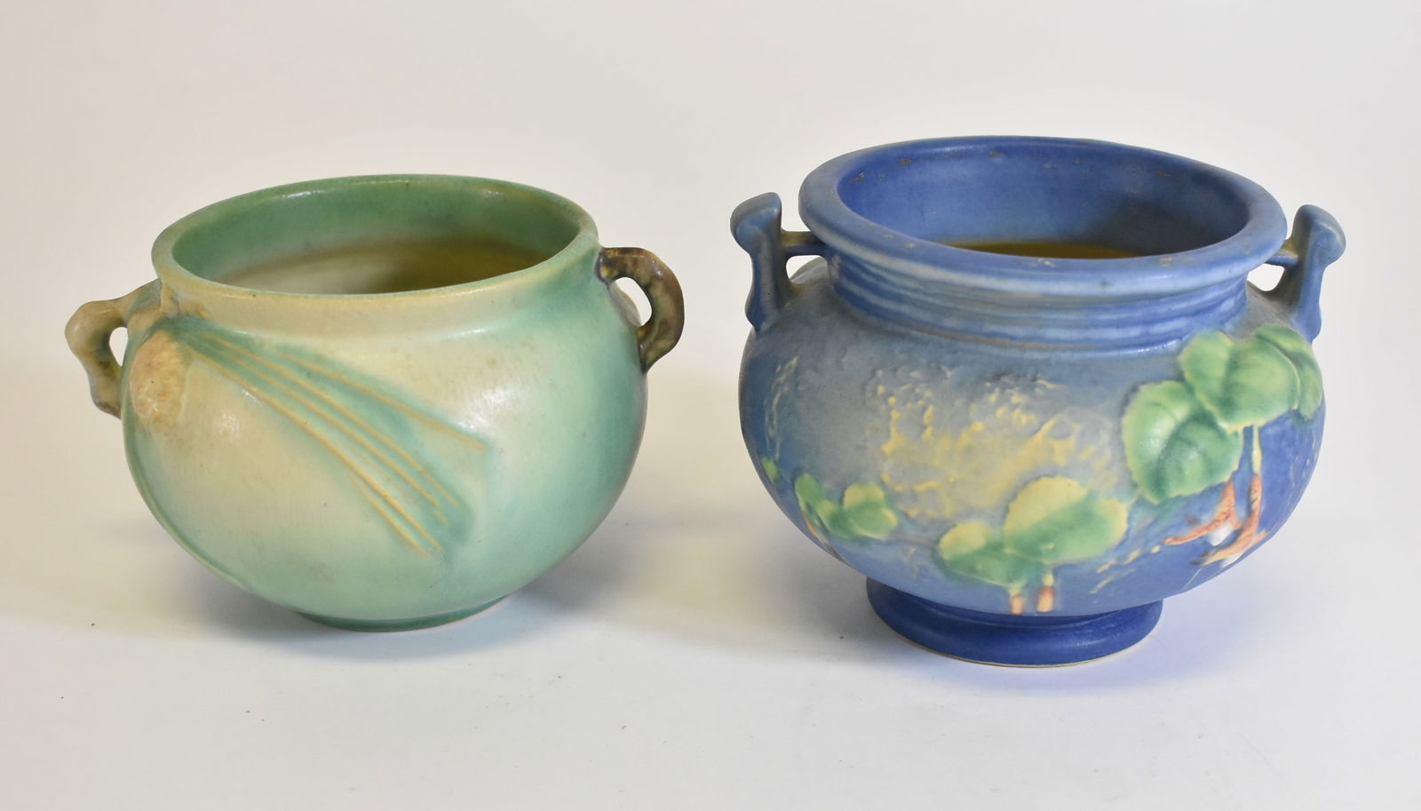 2 Roseville Pots Pinecone and Bleeding Hearts: Roseville green pinecone pot, 1931, 3" tall. Chip on the bottom. Blue bleeding heart pot, 4" tall. Marked on the bottom.