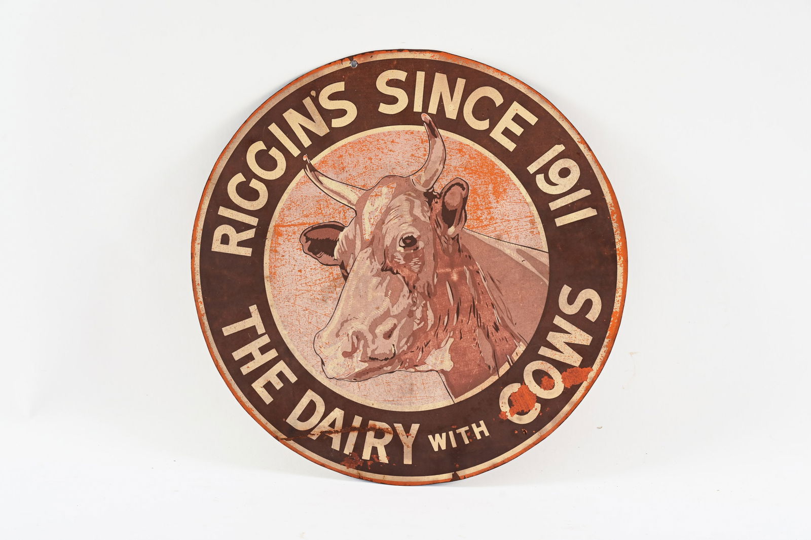 RIGGIN'S SINCE 1911 PAINTED METAL SIGN: RIGGIN'S SINCE 1911 "THE DAIRY WITH COWS" PAINTED METAL SIGN NOT MARKESD HAS BEEN CUT OUT OF A LARGER SIGN SHOWS WEAR, PAINT LOSS AND FADING IN FIELD SLIGHT BEND AT BOTTOM EDGE 14" *ALL ITEMS GUARANTE