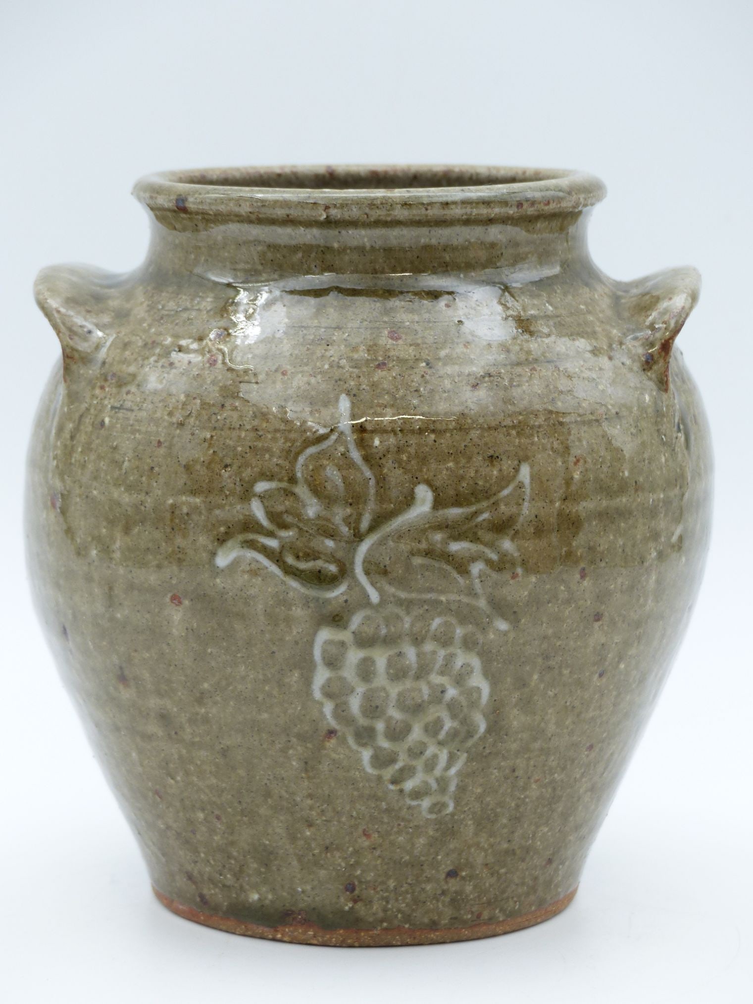 "Genevieve Storage Jar: This Genevieve Storage Jar is a charming example of functional pottery characterized by its earthy glaze and charming grape motif on the exterior. The jar exhibits a classic round shape with a wide op
