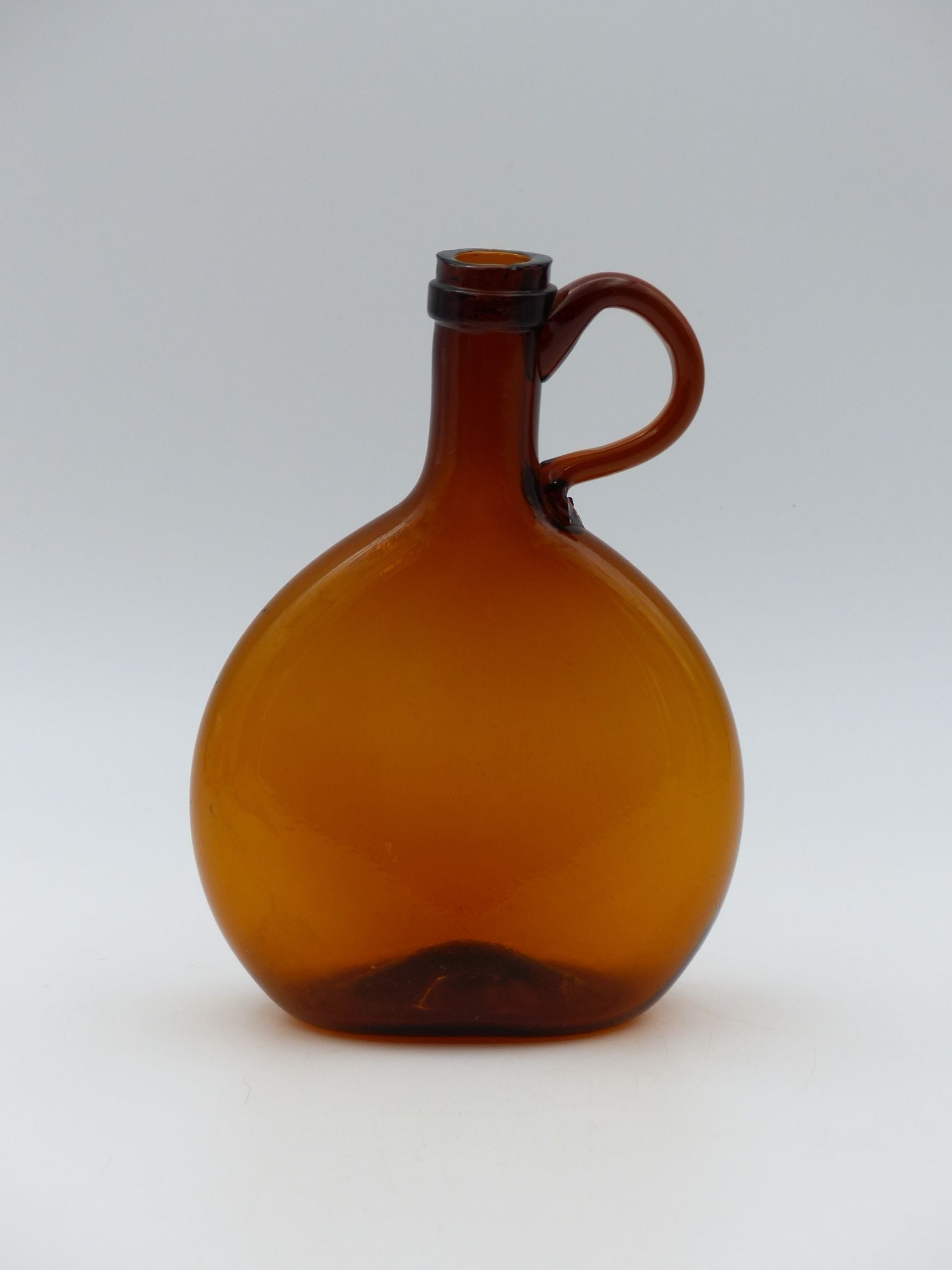 Amber Chestnut Bottle with Pontil (Mint): This exquisite amber chestnut bottle showcases a captivating design characteristic of the vintage glassware era. The bottle, with its rich chestnut hue, features a gracefully contoured body and a func