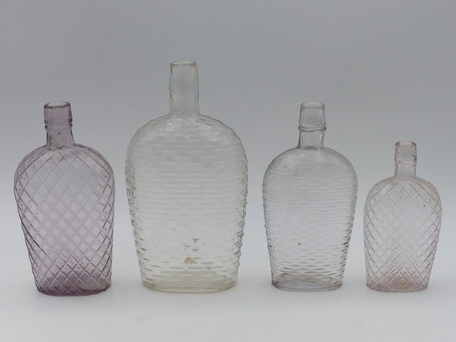 Web & Diamond Pattern Flask Collection: This exquisite collection features four flasks, each showcasing elegant diamond and web patterns. Crafted from glass, these flasks exhibit a refined aesthetic with their varied hues that range from so