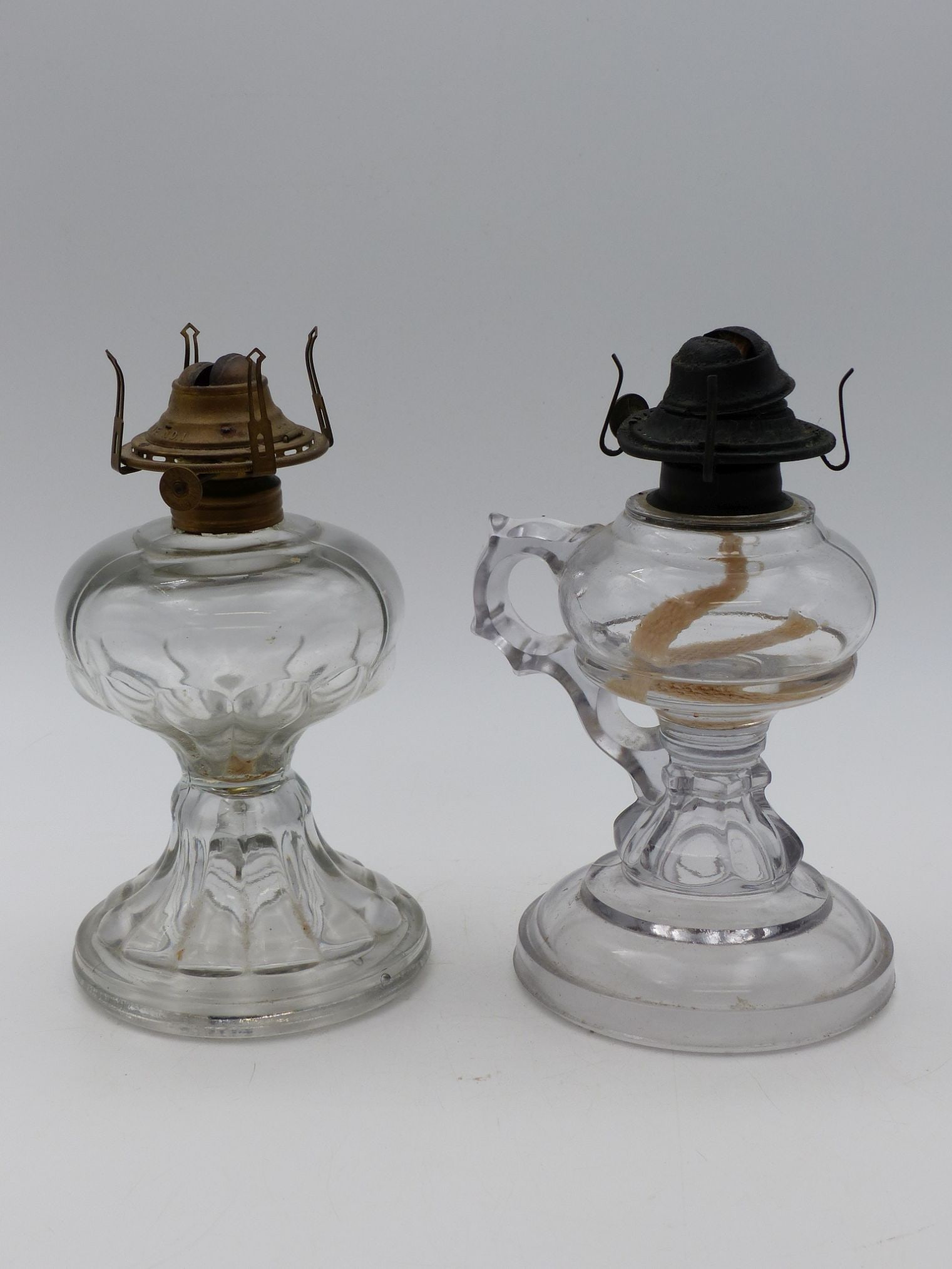 Finger Oil Lamp Pair (Excellent Condition): This exquisite pair of finger oil lamps exemplifies early 20th-century craftsmanship, showcasing elegant glasswork and intricate metal fittings. Each lamp features a distinct design, with one exhibiti