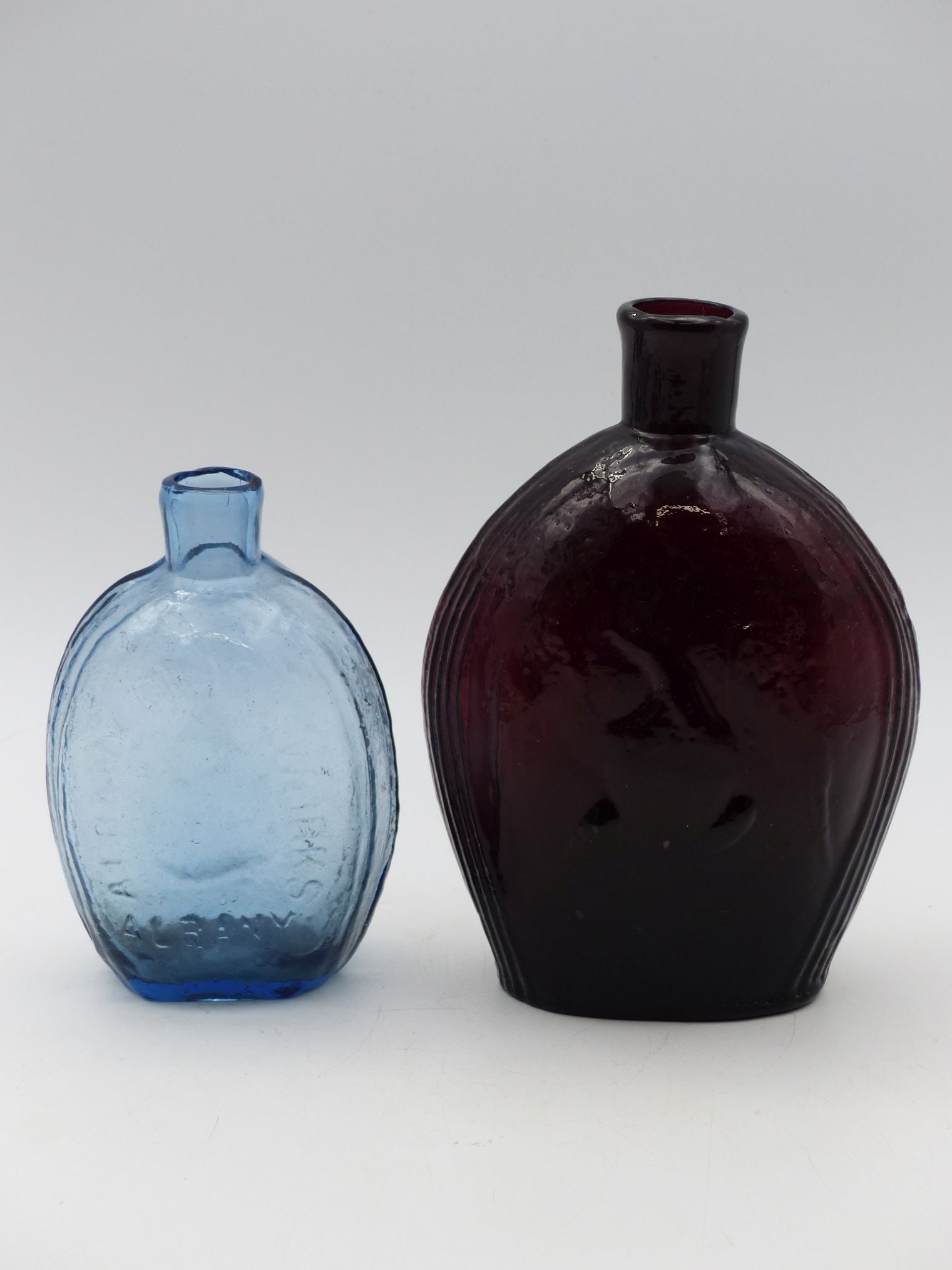 Union Flask Pair: Albany Glass Works & Amethyst Flasks: This striking pair of union flasks showcases craftsmanship from Albany Glass Works, featuring a vibrant blue flask and an amethyst flask. The blue flask exhibits a smooth surface with subtle texturing