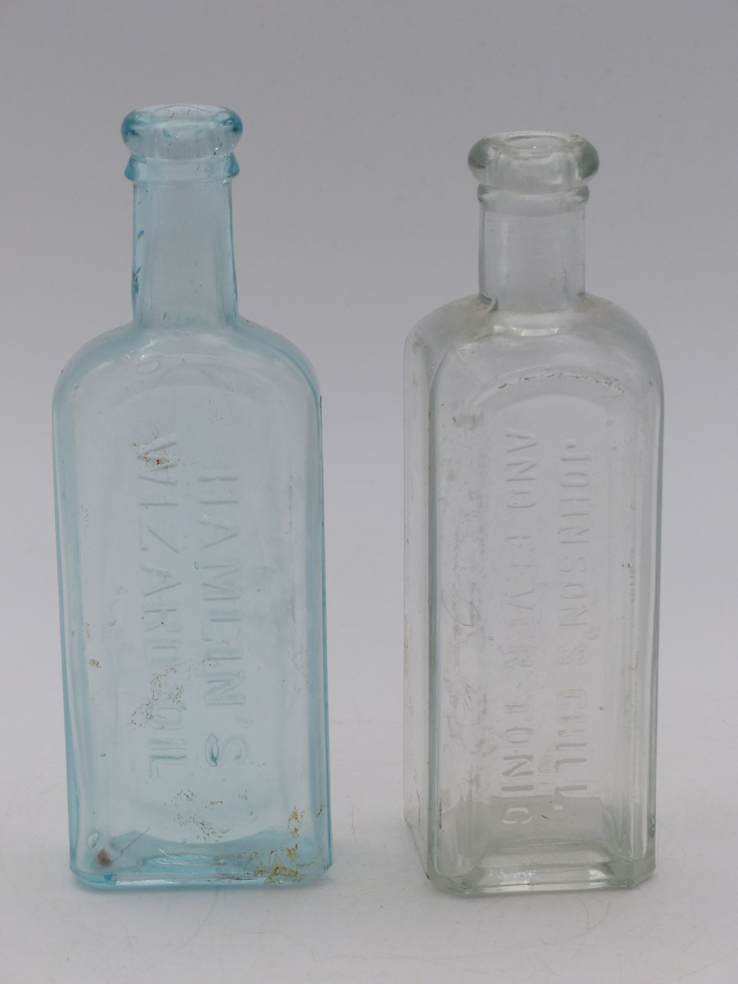 "Medicine Bottle Pair: Hamlin's Wizard Oil: This striking pair of medicine bottles includes Hamlin's Wizard Oil, an iconic patent medicine popular from the late 19th century. The left bottle is characterized by its distinct blue tint and emboss