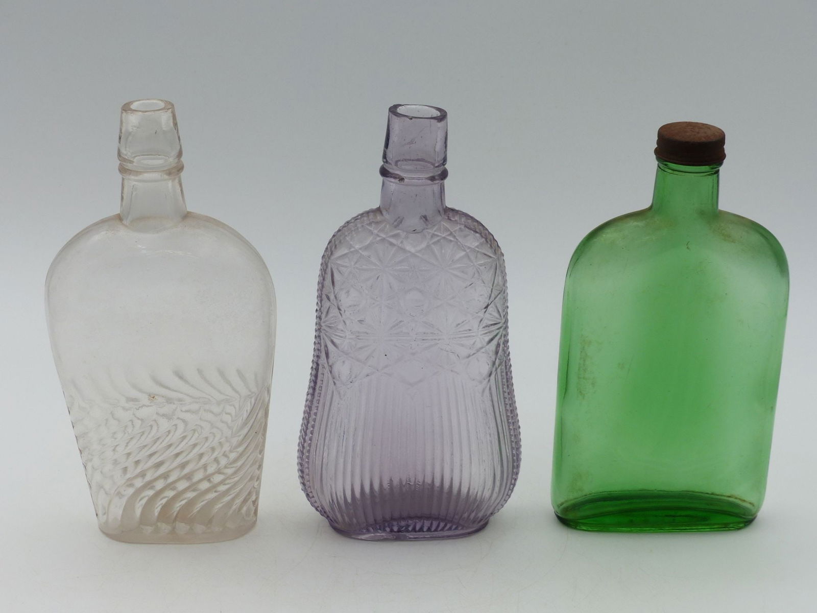 "Whiskey Flask Collection: Spider: This exquisite collection of whiskey flasks showcases a distinctive assortment comprising three beautifully crafted glass flasks, each exhibiting unique design elements. The centerpiece is a curvaceou