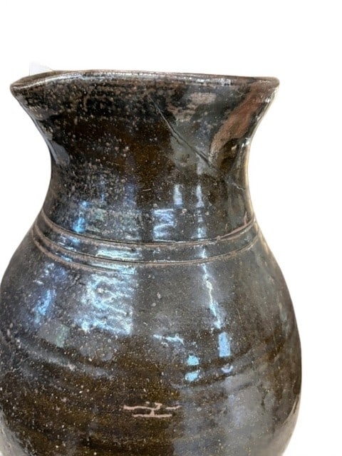 Rustic Salt-Glazed Stoneware Pitcher with Applied Handle: This antique salt-glazed stoneware pitcher features a deep, mottled brown finish and a sturdy, hand-applied handle. The vessel shows an elegant baluster form with distinct horizontal incised lines dec