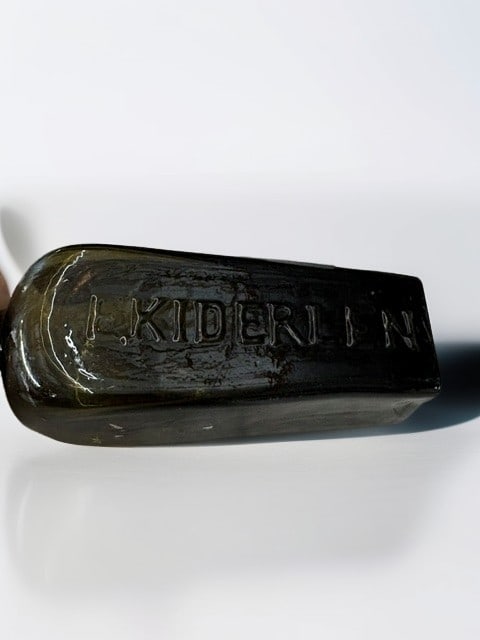 Antique Olive Green Embossed Glass Medicine Bottle: This antique, free-blown, deep olive green glass medicine bottle features a tapered rectangular shape and is distinctly embossed with the name E. KIDERLEN. The bottle showcases desirable characteristi