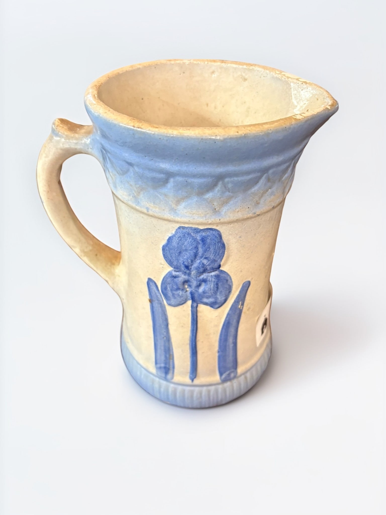 Antique Blue and White Salt-Glazed Stoneware Pitcher: This charming antique stoneware pitcher features a classic blue and white color scheme with a hand-painted floral motif. The vessel is designed with a textured, molded band around the rim and base, pr