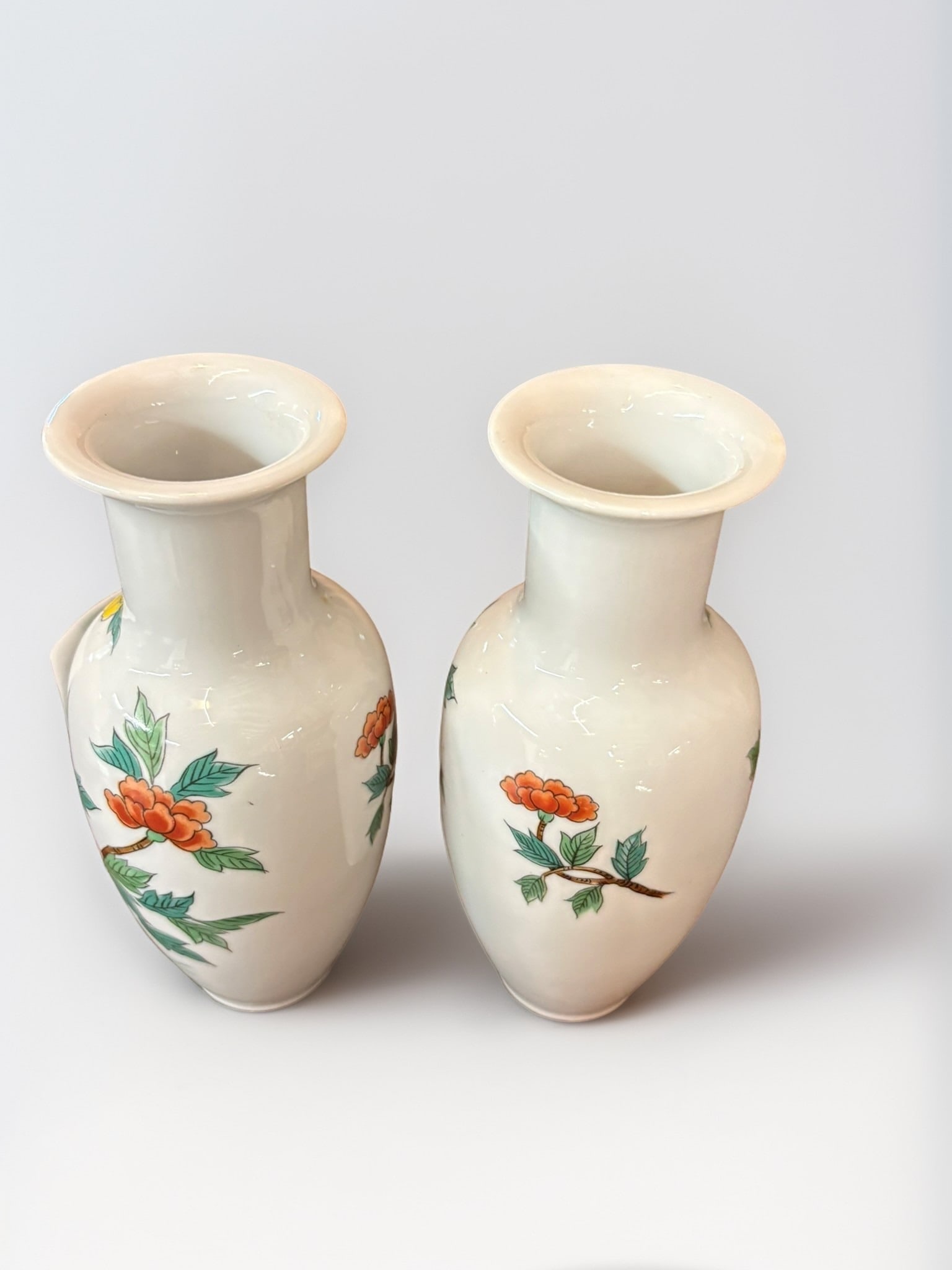 Pair of Famille Rose Style Porcelain Floral Vases: This elegant pair of porcelain vases features delicate hand-painted floral motifs in the Famille Rose palette, showcasing vibrant orange, yellow, and pink peonies against a crisp white ground. The vas