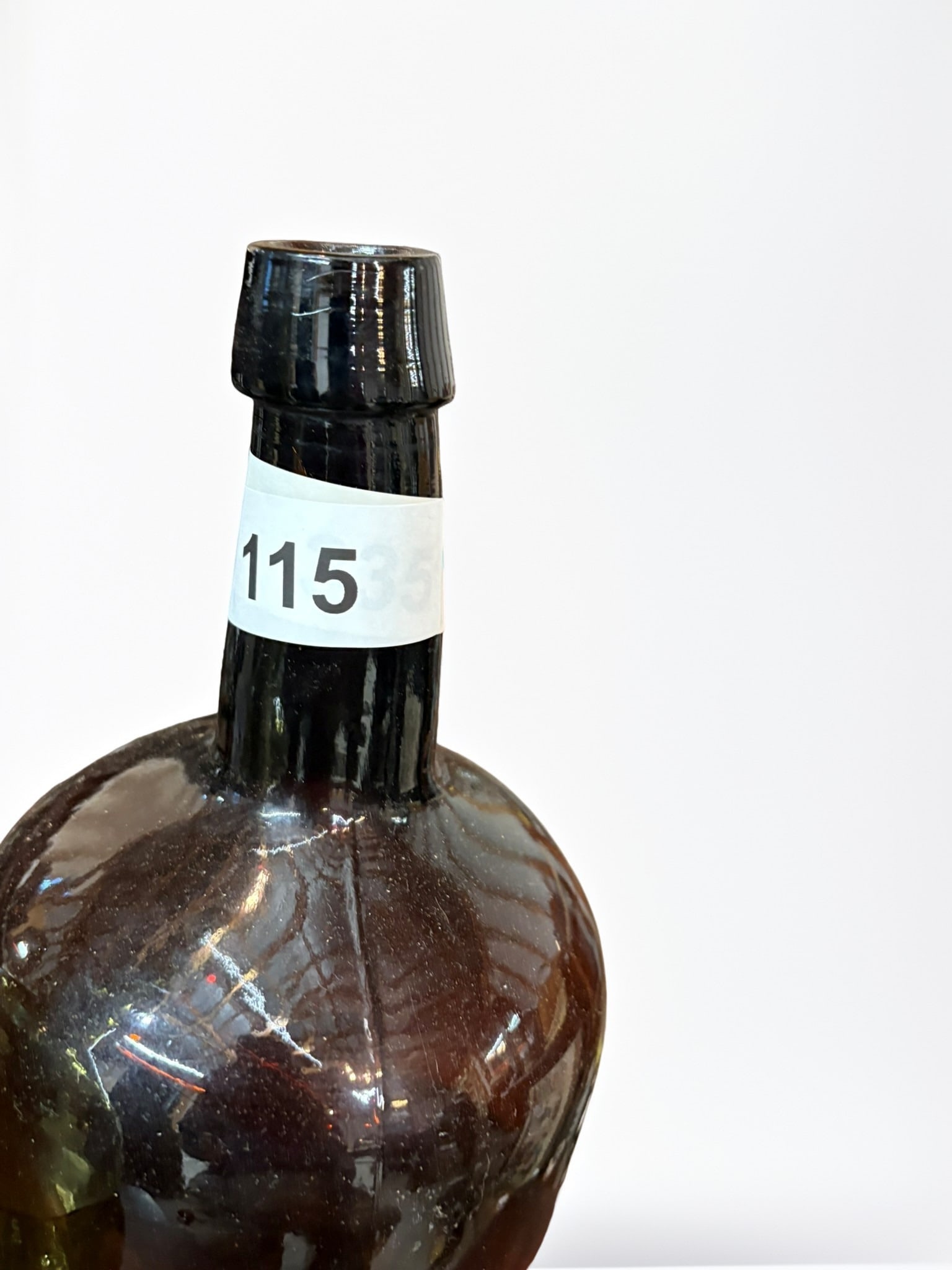 Pair of Antique Hand-Blown Glass Demijohns: A decorative pair of substantial, antique hand-blown glass demijohn bottles. One bottle features a classic olive-green hue, while the other is in a deeper amber-brown glass. Both exhibit charming impe