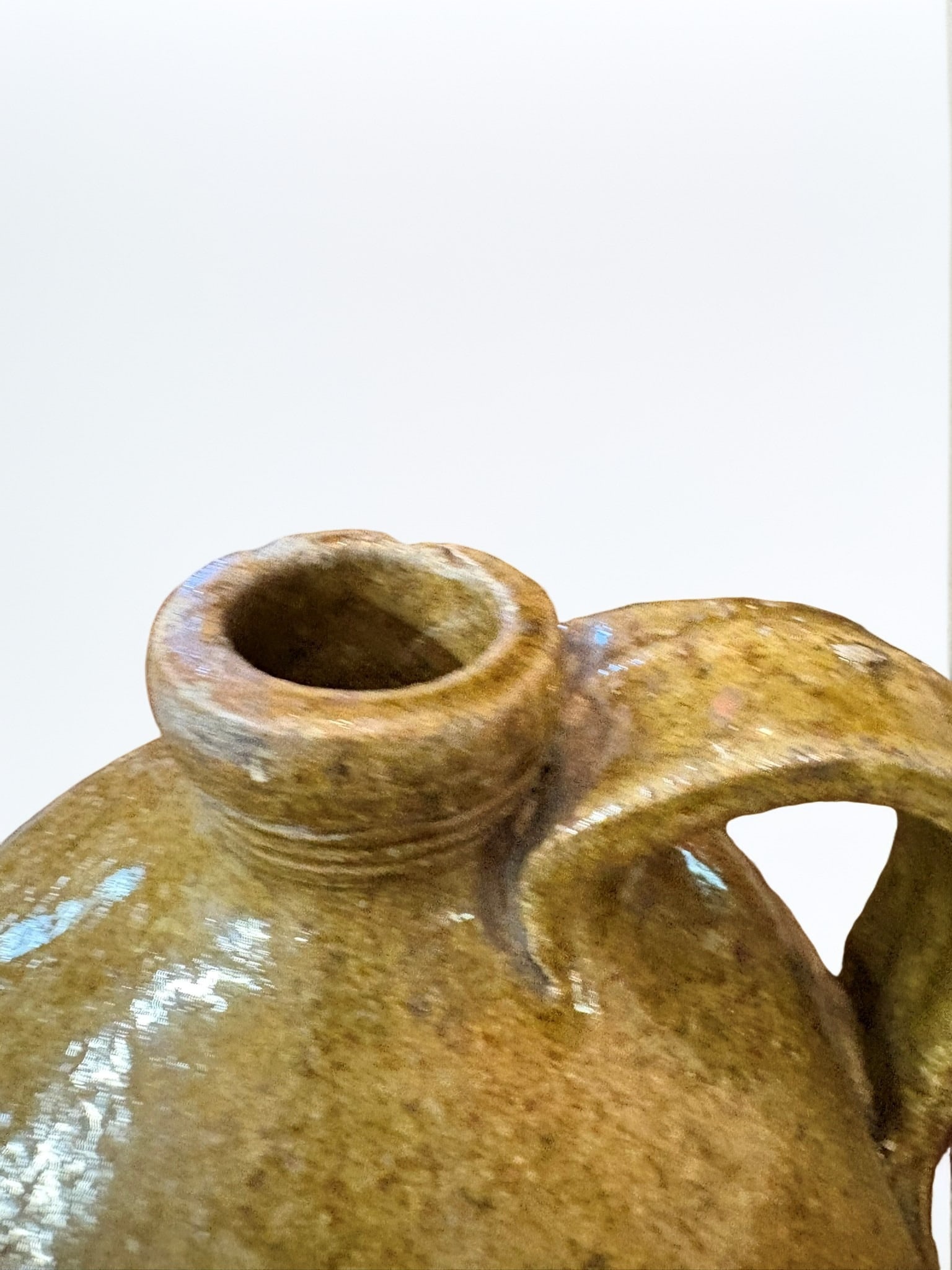 Southern Alkaline Glazed Stoneware Jug: A traditional American Southern alkaline glazed stoneware jug, featuring a classic ovoid form with a simple strap handle and an applied collar rim. The piece displays a characteristic mottled