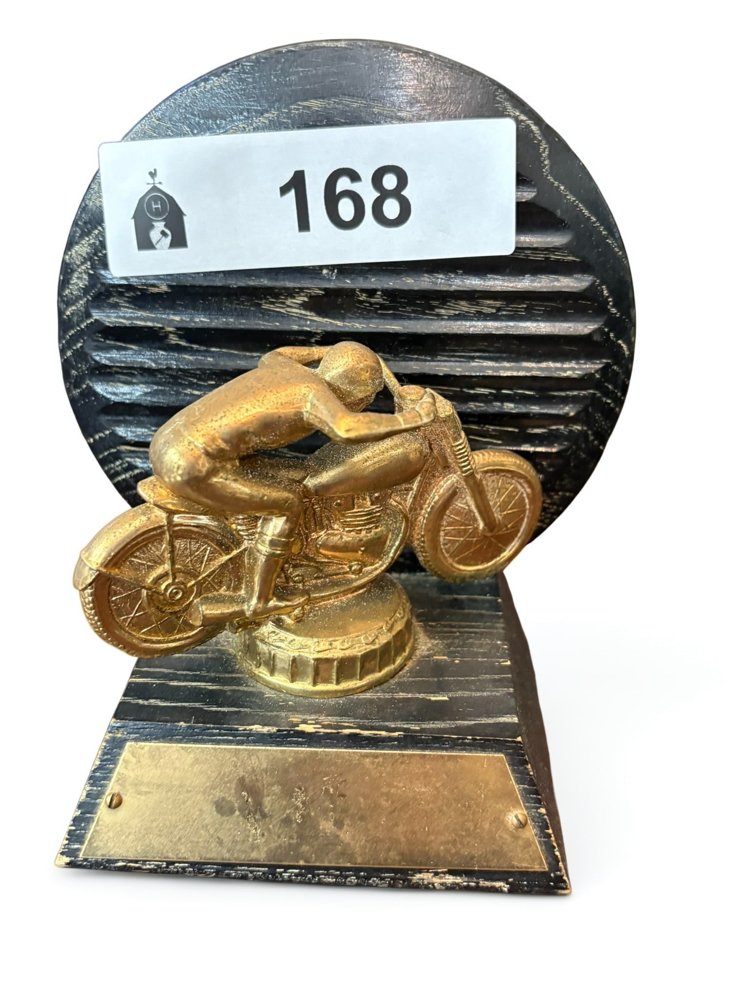Vintage Motorcycle Racing Achievement Trophy: This vintage motorcycle racing trophy features a gold-toned plastic figure of a racer in a competitive crouch, mounted upon a circular wooden backing with a textured, burnt-wood finish. The base inclu