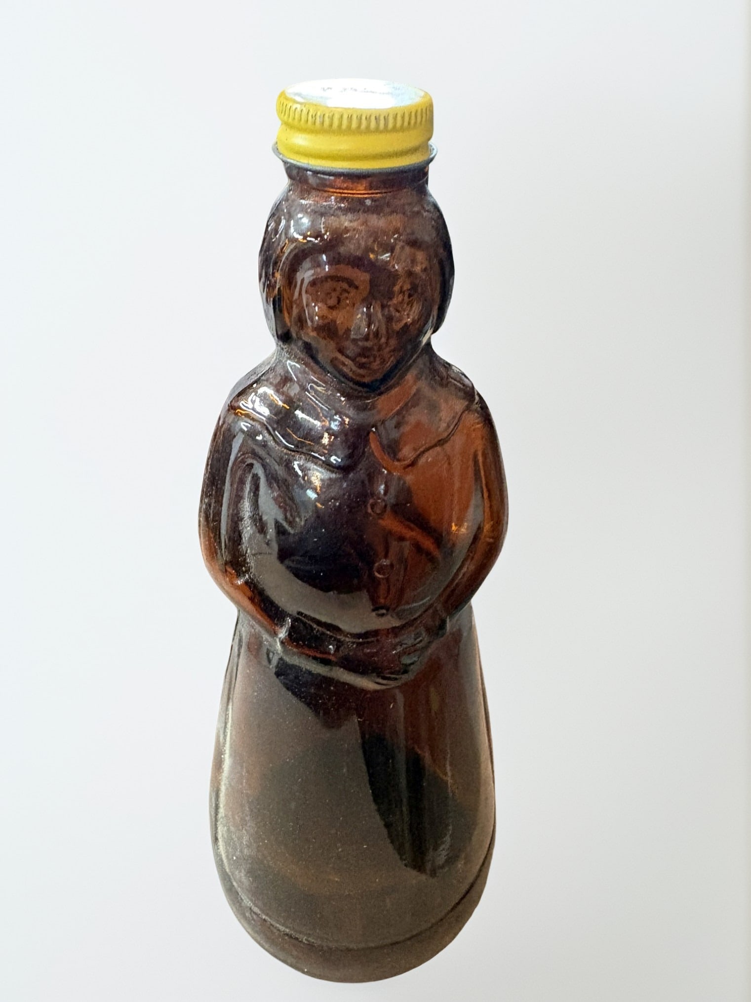 Pair of Vintage Amber Glass Containers: Syrup Bottle and Jug: This lot features a charming pair of mid-to-late 20th-century amber glass containers. Included is a figurative syrup bottle shaped like a woman in a bonnet, paired with a standard round amber glass