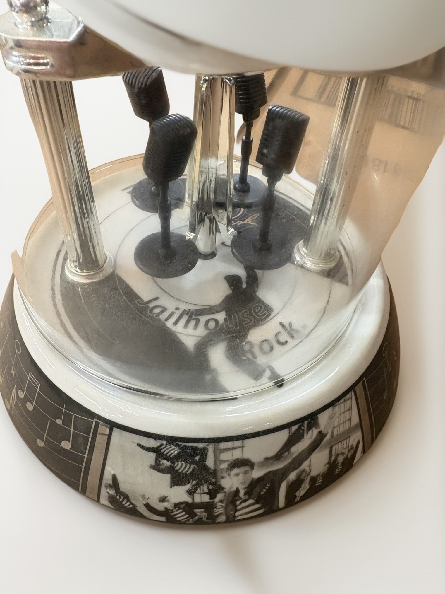 Elvis Presley Jailhouse Rock Commemorative Desk Clock: This collectible desk clock features an iconic black-and-white portrait of Elvis Presley and is housed under a clear protective dome. The base is decorated with scenes from his legendary 'Jailhouse
