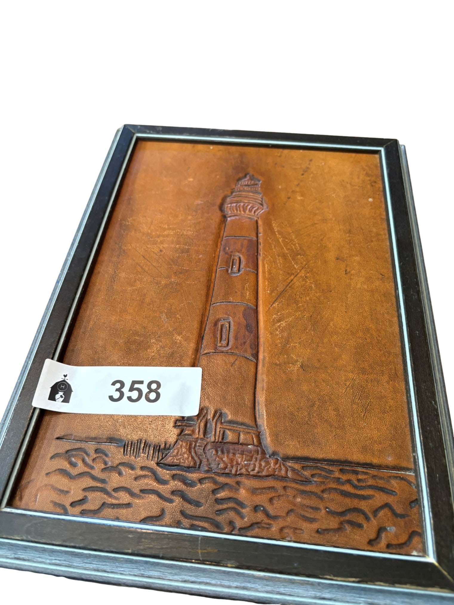 Vintage Hand-Tooled Leather Lighthouse Wall Plaque: This vintage wall plaque features an intricately hand-tooled leather relief depicting a coastal lighthouse. The artisan has captured the architectural detail of the structure and the texture of the su