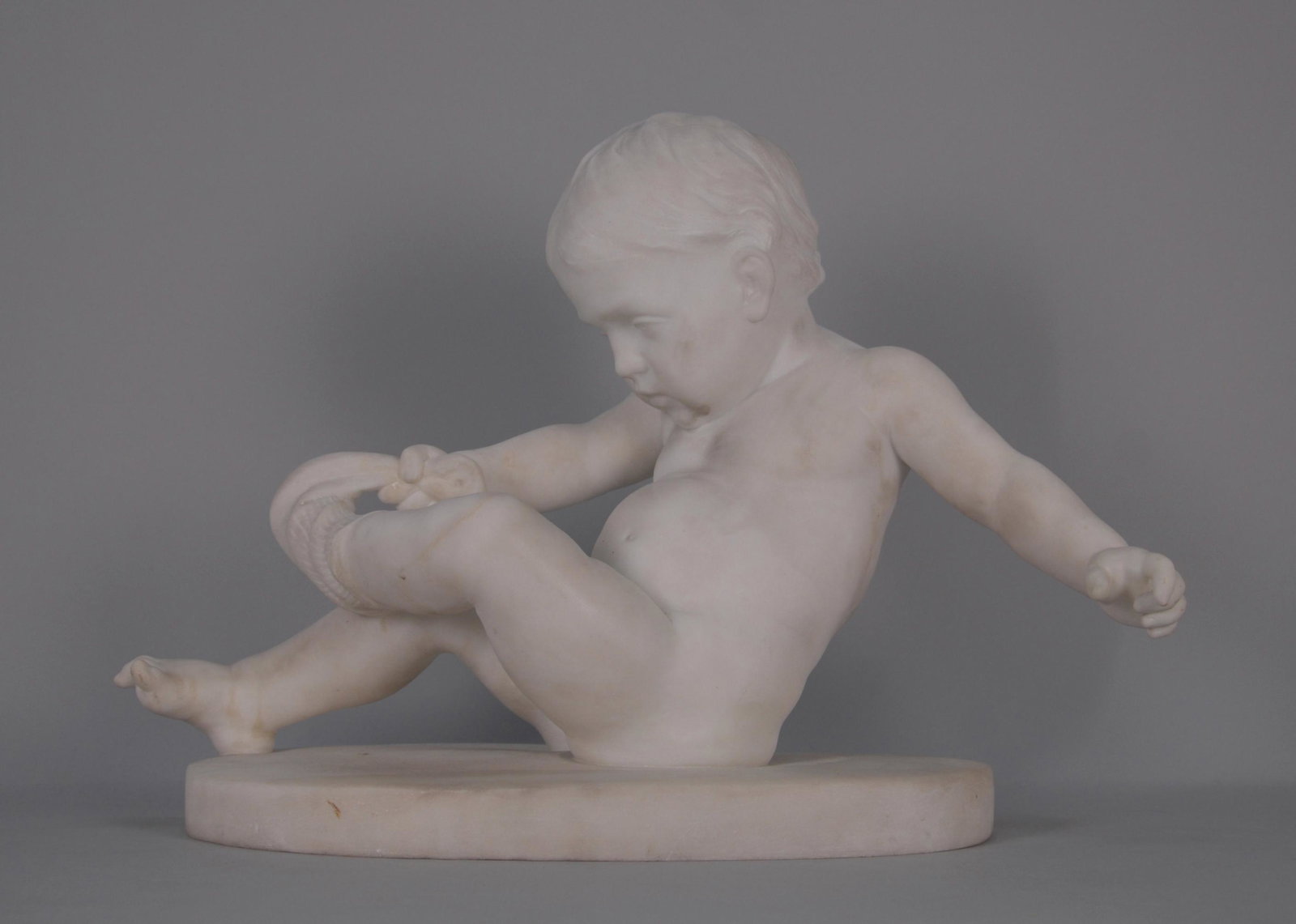 LAZZERINI ALESSANDRO. Scultura in marmo.: LAZZERINI ALESSANDRO - Carrara, 1860-1942. Scultura in marmo statuario raff. ''BAMBINO CHE SI TOGLIE UNA CALZA''. Firmata alla base. Mis. Lung. cm. 56 Alt. cm. 40 Prof. cm. 24.5 ca. Val. 1000/1600