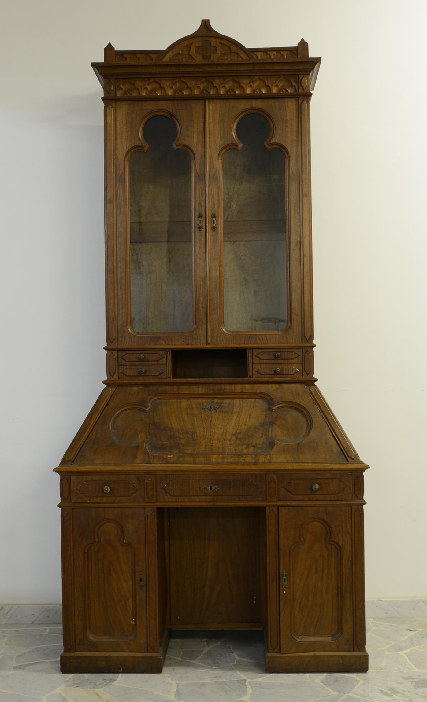 Wooden trumeau. Liberty period: Trumeau in noce con parte superiore a due ante in vetro su scomparto e cassettini. Parte inferiore con ribalta su tre ante a pannello. Periodo Liberty. Mis. Lung. cm. 115 Alt. cm. 252 Prof. cm. 54 ca.