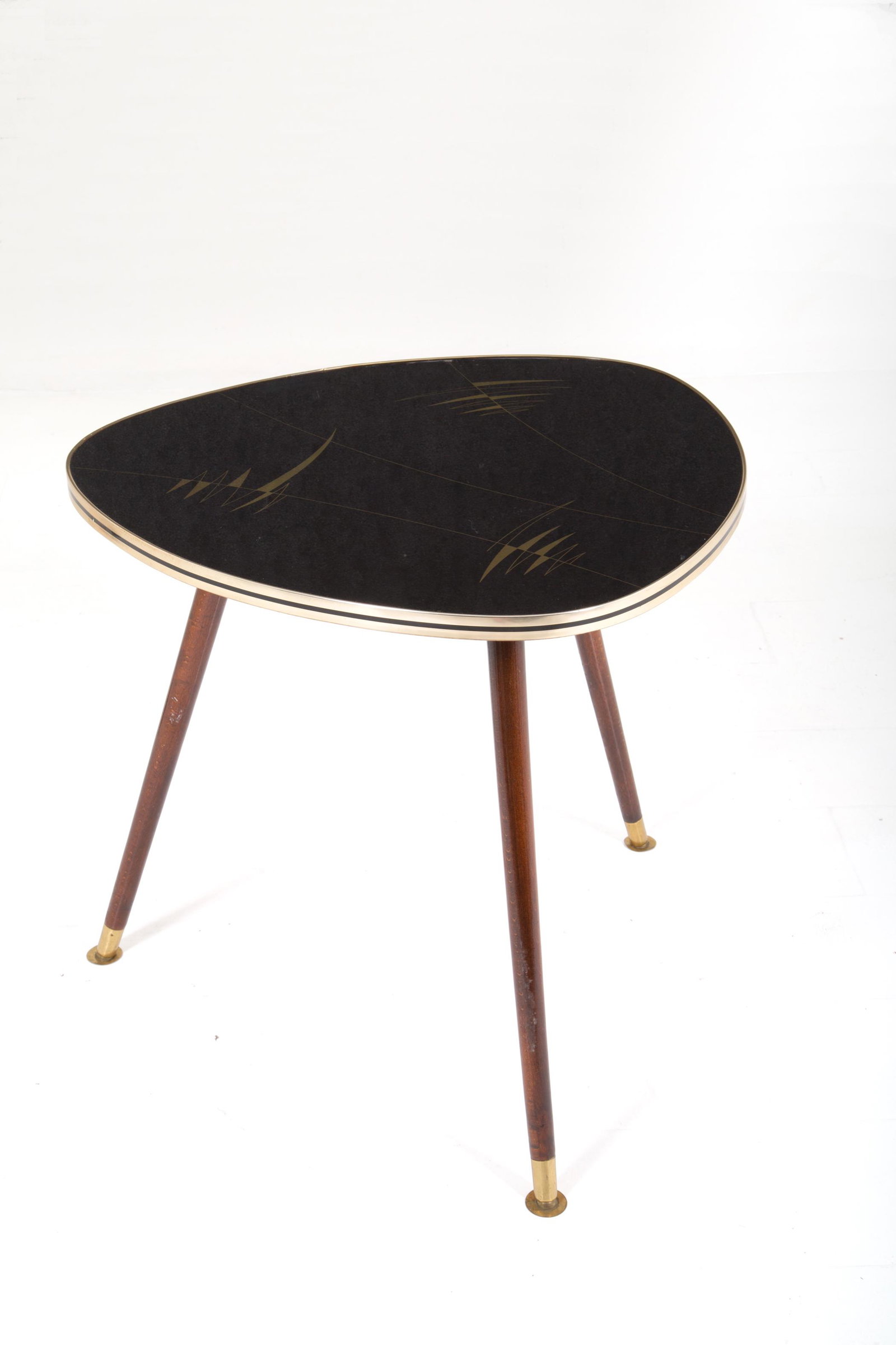 Triangular wooden coffee table with three legs: Tavolino triangolare in legno a tre gambe. Piano nero con decoro astratto dorato rivestito da cristallo e angoli smussati. Profilature e piedini in ottone. Manifattura italiana. Anni '50-'60. Mis. Lun