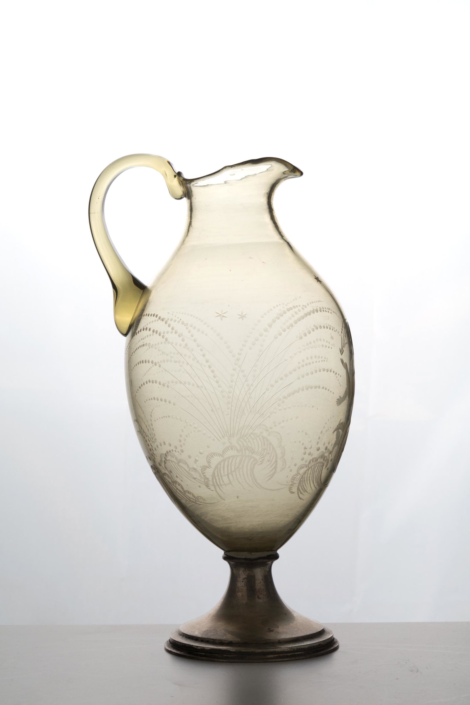 GUIDO MARIA BALSAMO STELLA.Glass and silver pitcher: GUIDO MARIA BALSAMO STELLA (Torino, 1882 - Asolo, 1941). Brocca in vetro con base in argento 800. Mis. Lung. cm. 16 Alt. cm. 27.5 Diam. cm. 14 ca. Val. 800/1000