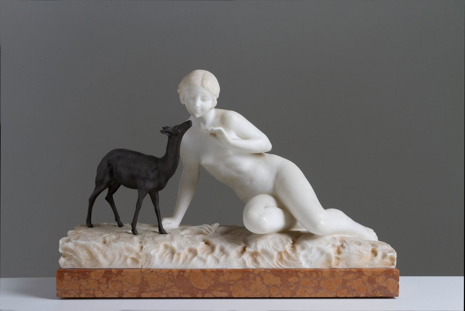 UMBERTO STIACCINI. Sculpture "NUDE OF LADY WITH FAWN'': Alabaster and burnished bronze sculpture depicting '' NUDE OF LADY WITH FAWN ''. France red marble base. Signed on the back. Early 20th century. Right hand restoration. 30x49x18 cm approx. Scultura in