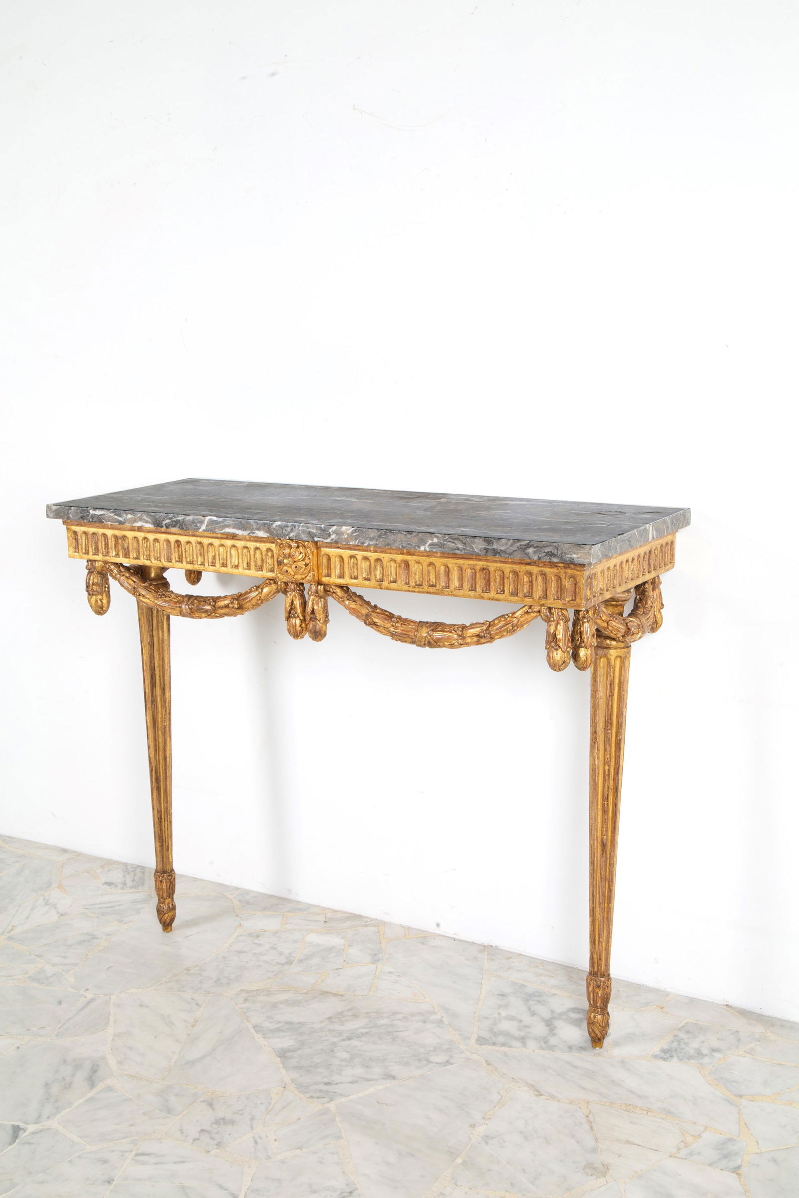 Console table with marble top: Carved and gilded wood console table with fluted legs and a gray marble top. Louis XVI period. 93x110x41.5 cm approx. Consolle in legno intagliato e dorato con gambe scanalate e piano in marmo grigio.
