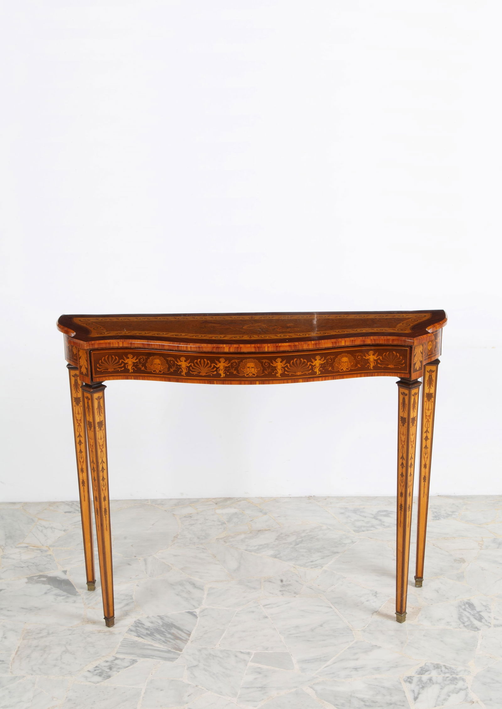 Console table. In Louis XVI style: Console table veneered and inlaid in various woods with grotesque motifs on the legs and decorations on the shaped top. Pyramidal legs with brass tips and a drawer on the side. Louis XVI style. Early