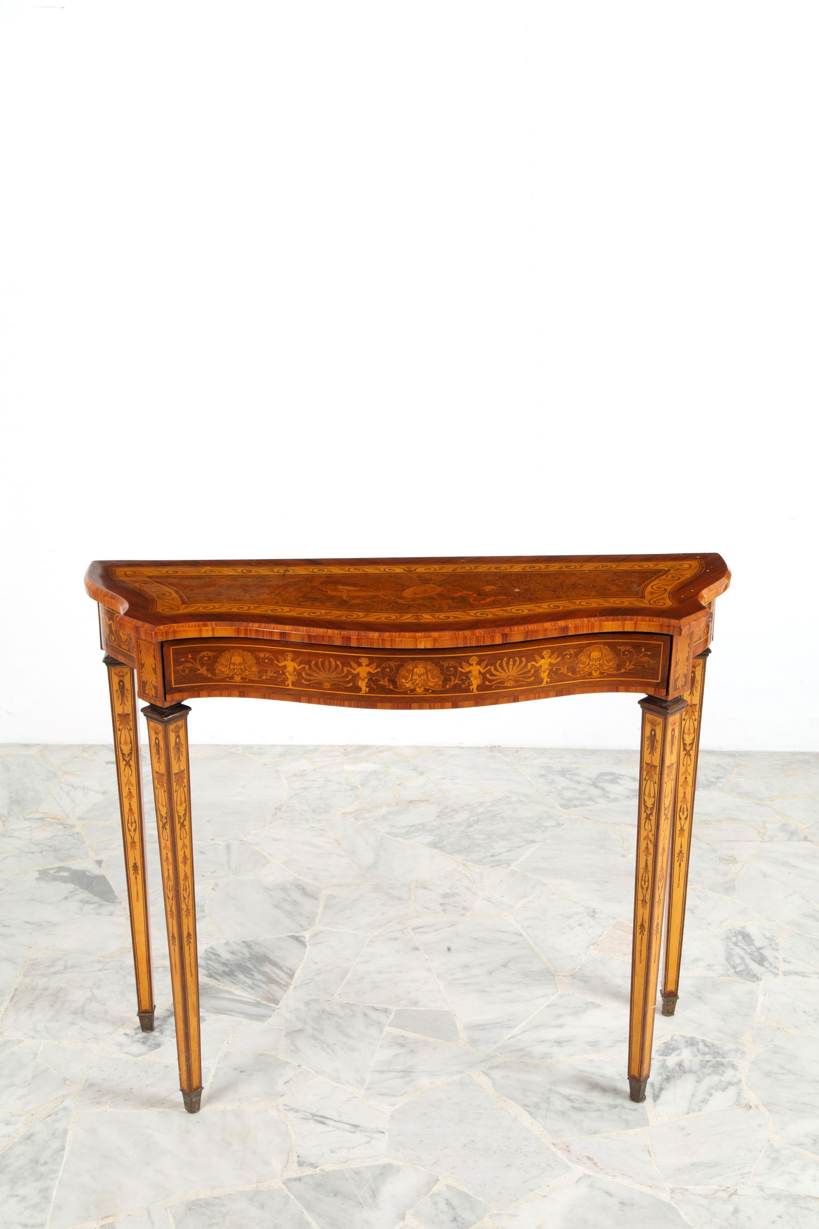 Console table. In Louis XVI style: Console table veneered and inlaid in various woods with grotesque motifs on the legs and decorations on the shaped top. Pyramidal legs with brass tips and a drawer on the side. Louis XVI style. Early
