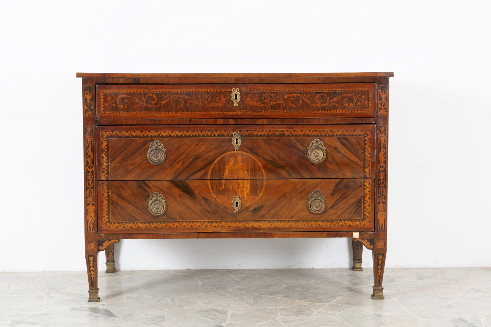 Como': Three-drawer chest of drawers, finely inlaid with various woods and rose windows on the sides and top. Finely chiseled and gilded bronze fittings. Louis XVI period. Some defects and missing parts.