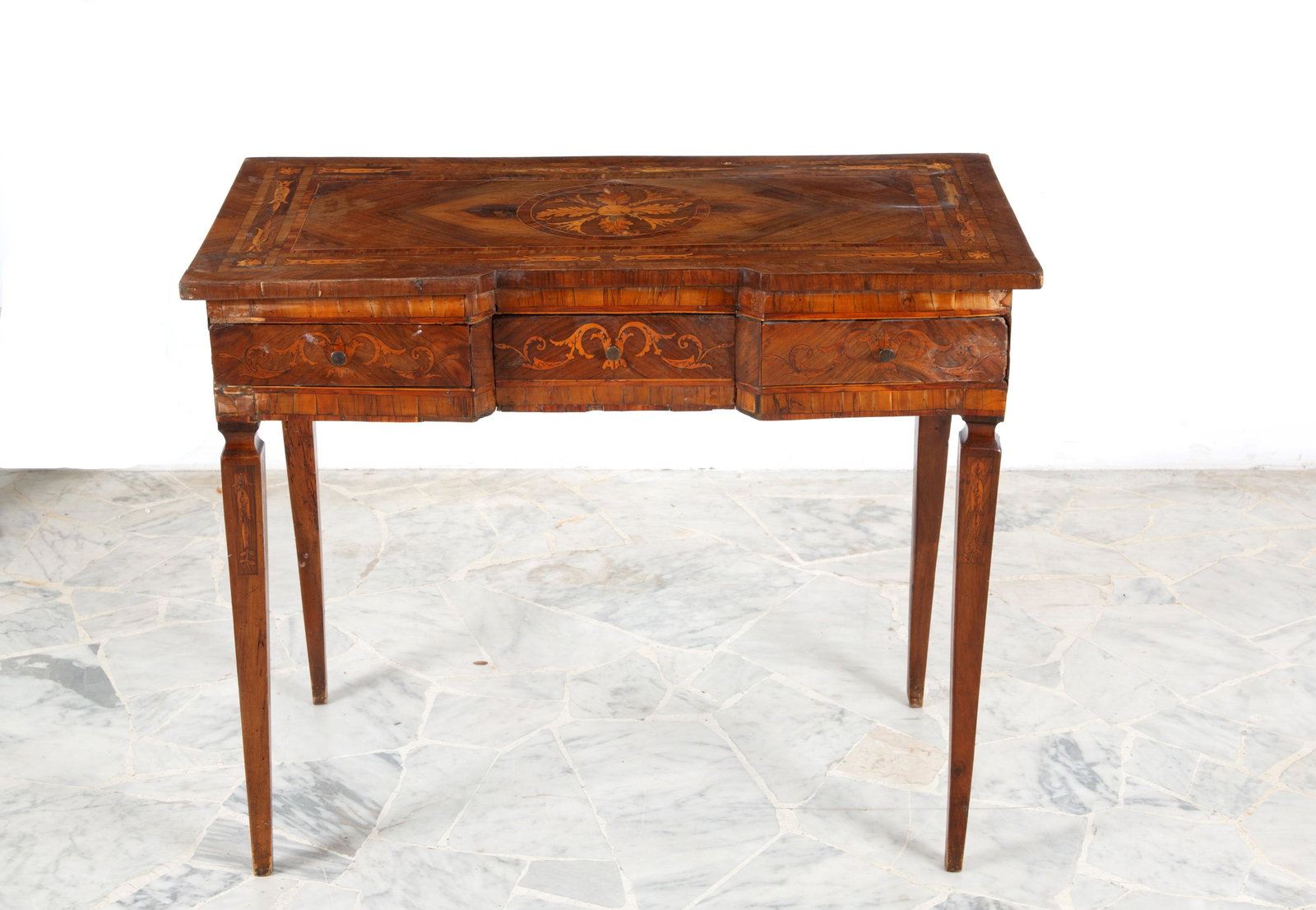 Scrittoio intarsiato: A veneered wooden writing desk, inlaid with various woods in floral and geometric motifs, with a rose window on the top, three drawers on the side and pyramidal legs. 19th century. Defects and