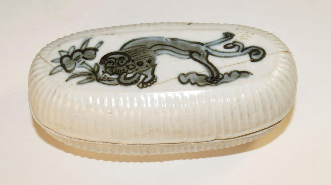 Chinese Blue and white covered box (l. 14 cm), Ming: Light grey stoneware, underglazed black-blue decoration, white-grey matt glaze, bottom and inside with glaze. Oval, thick-walled form on a low foot, ribbed wall, two compartments inside, h. 6 cm. Lion