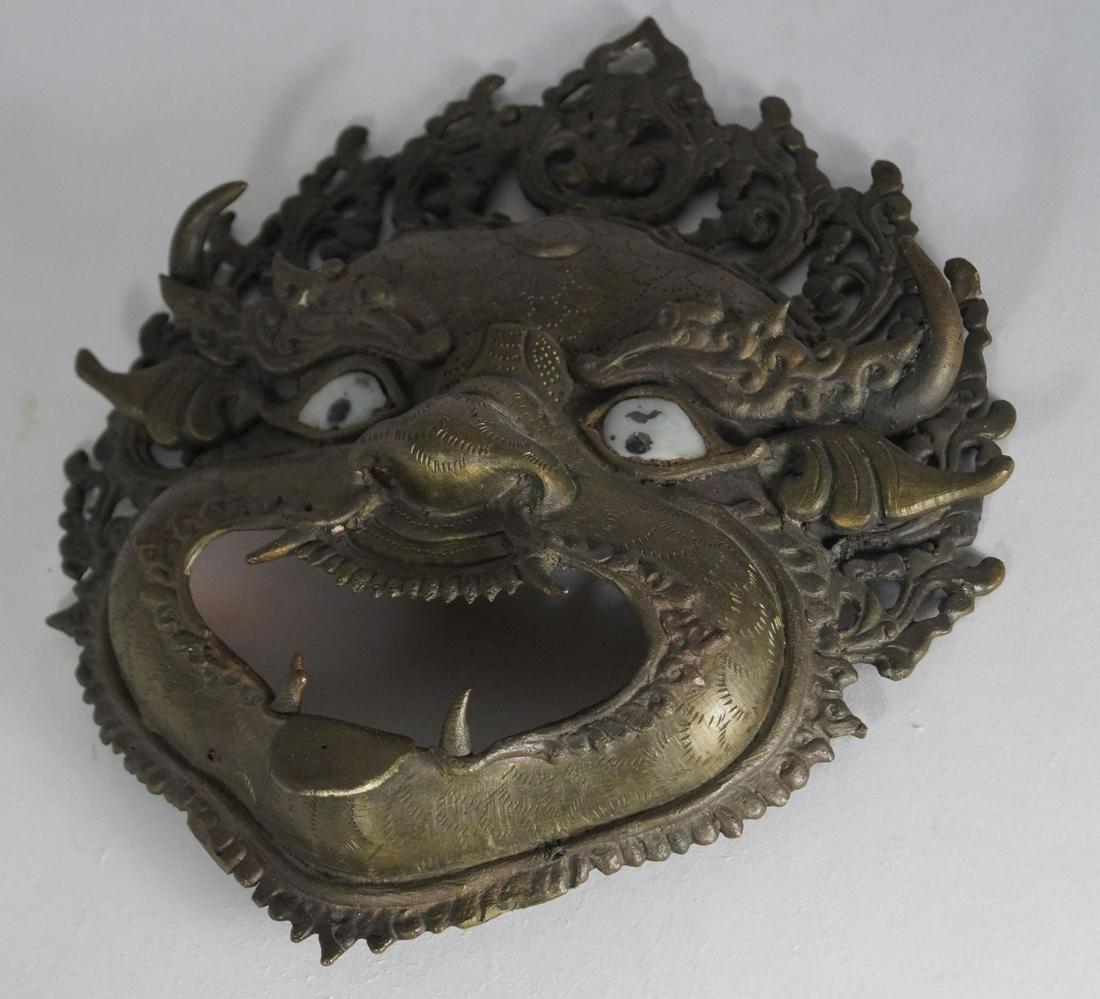 Chinese Guard mask, Nepal: Bronze, glass eyes, h. 23,5 x w. 20 cm. Demonic face with horns, open mouth and long fangs, pierced flame rim. (327)