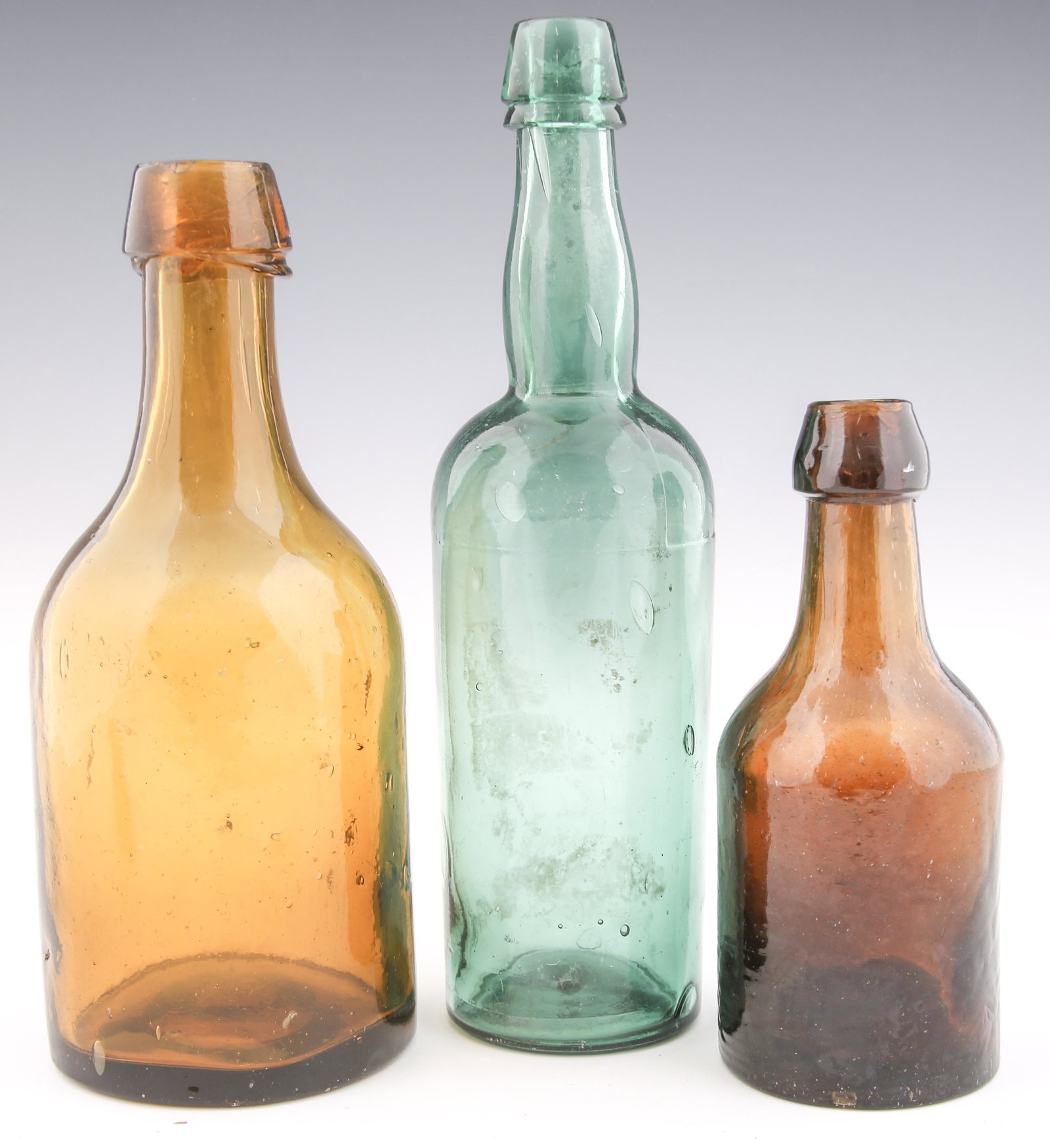 19TH C. GLASS BOTTLES - LOT OF 3: 19TH C. GLASS BOTTLES - LOT OF 3 Lot of three 19th century glass bottles. Includes: Dark amber bottle with whittled neck, applied top and dimpled pontil. Measures 6.75" tall and 2.75" in diameter. Lig