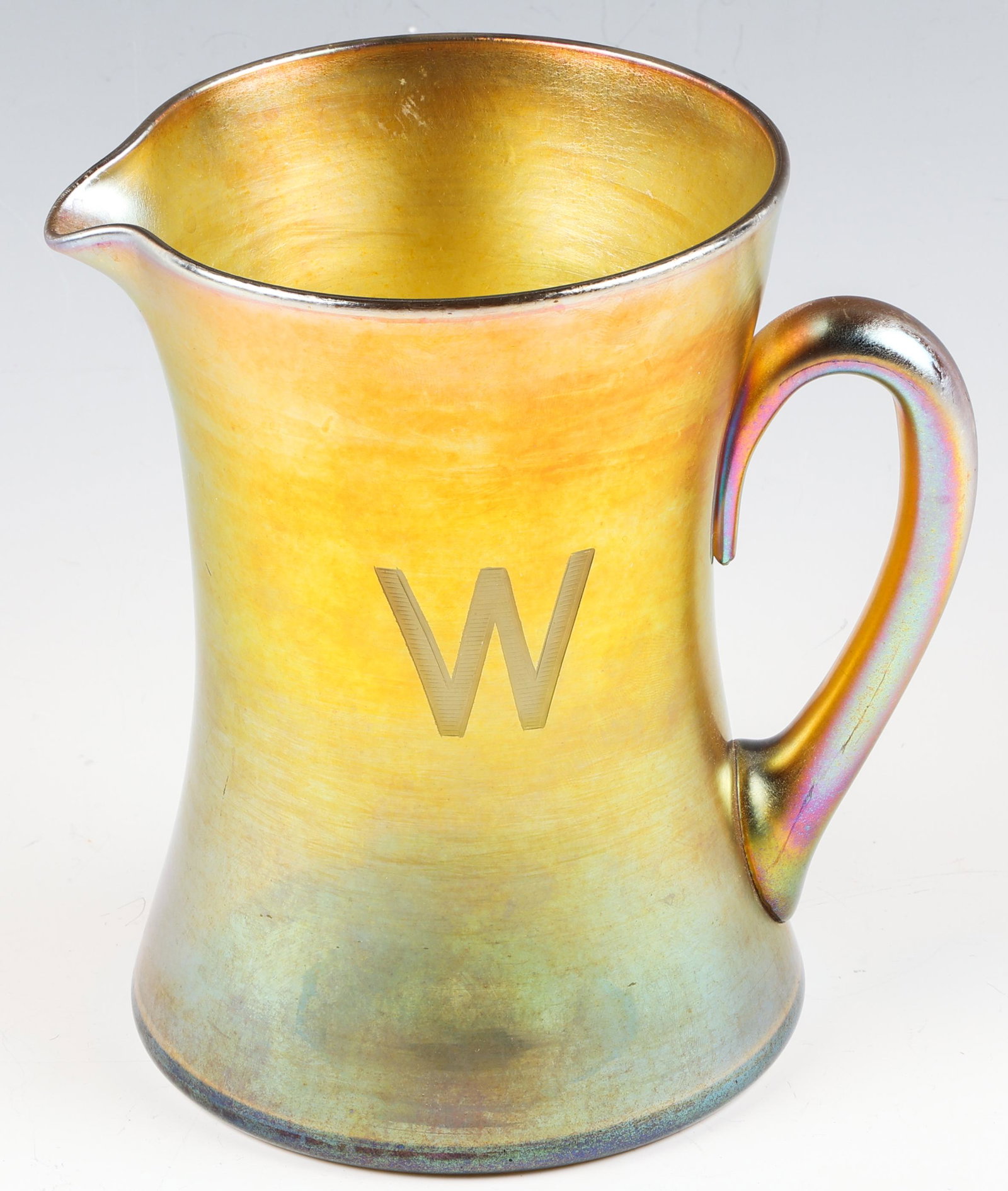 SIGNED TIFFANY STUDIOS FAVRILE GLASS PITCHER: SIGNED TIFFANY STUDIOS FAVRILE GLASS PITCHER Early 20th century Tiffany Studios favrile glass pitcher. Etched "W" design on side. Signed "L.C Tiffany Favrile" on bottom. Measures 6.25" tall and 4