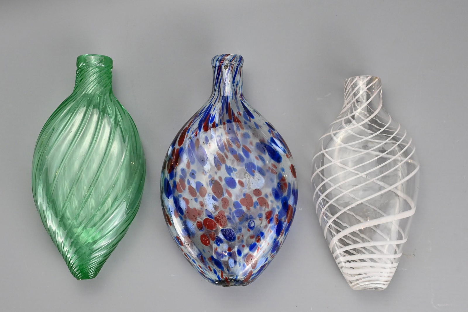 Three Bristol Nailsea Glass Flasks, 19th Century, one: Three Bristol Nailsea Glass Flasks, 19th Century, one clear glass decorated with white spiral trailing, one twisted green glass and one clear glass with blue and red mottled spots, largest 18.5 cm tal
